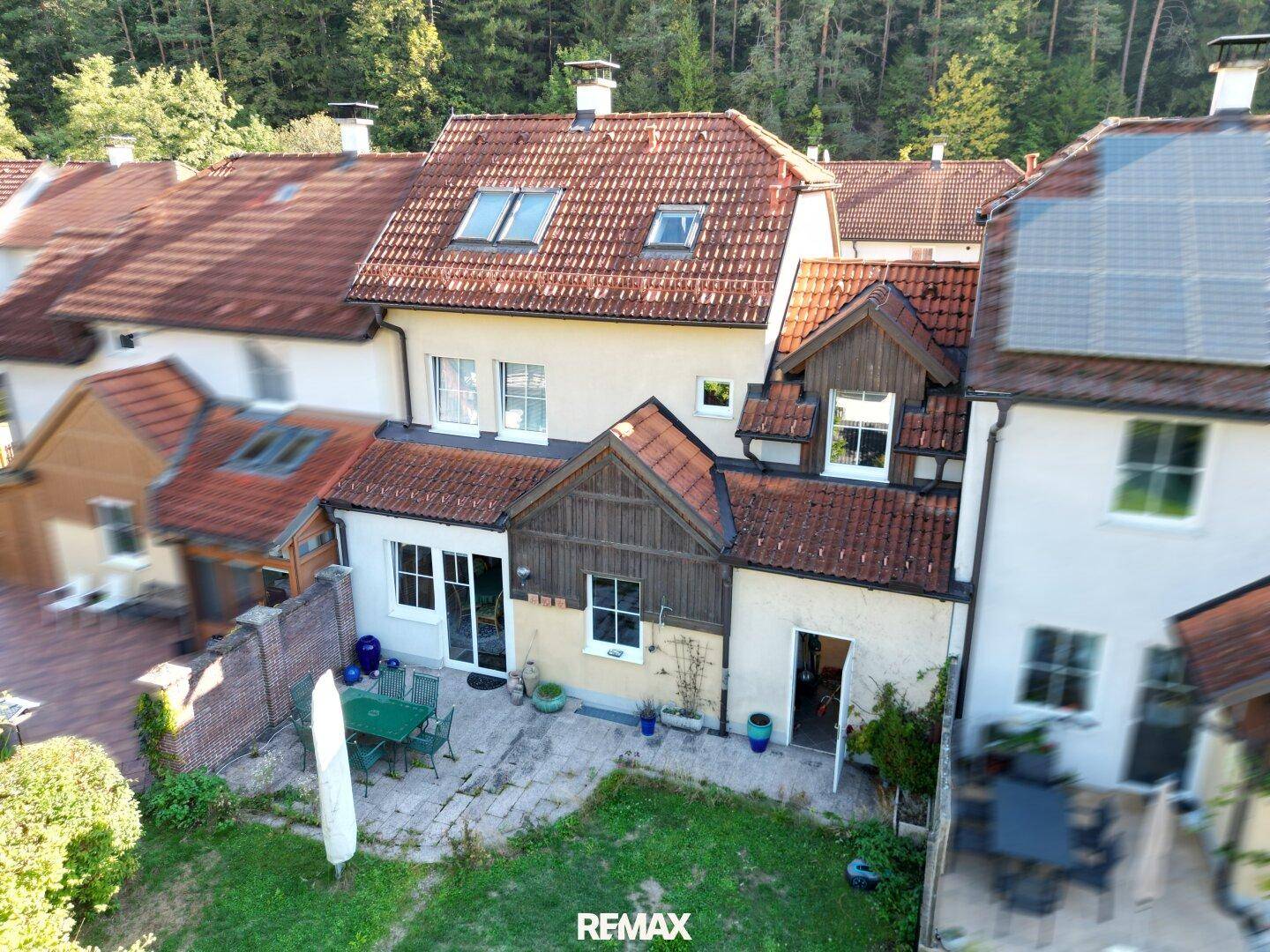 Rückansicht des Hauses mit Terrasse, Garten und Blick auf die bewaldeten Hügel.
