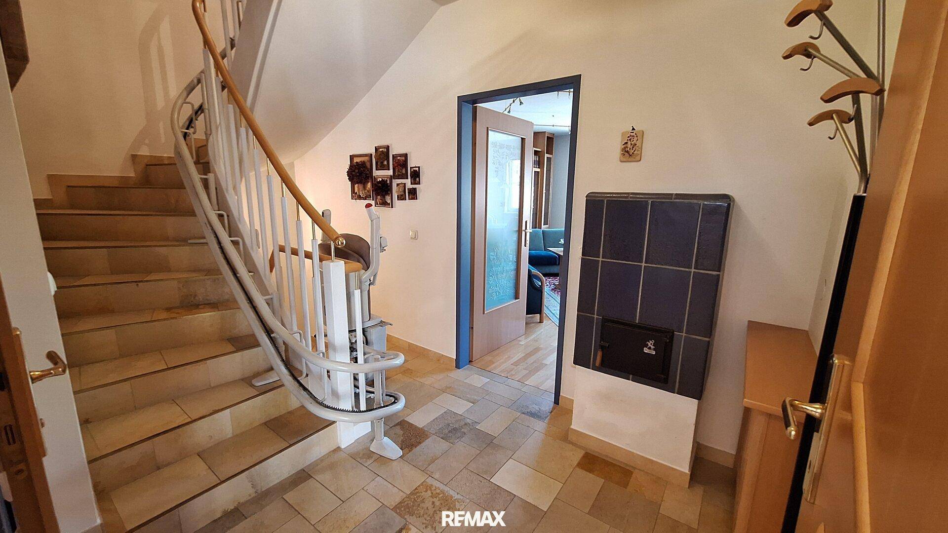 Eingangsbereich mit gefliester Treppe, Treppenlift und traditionellem Kachelofen.