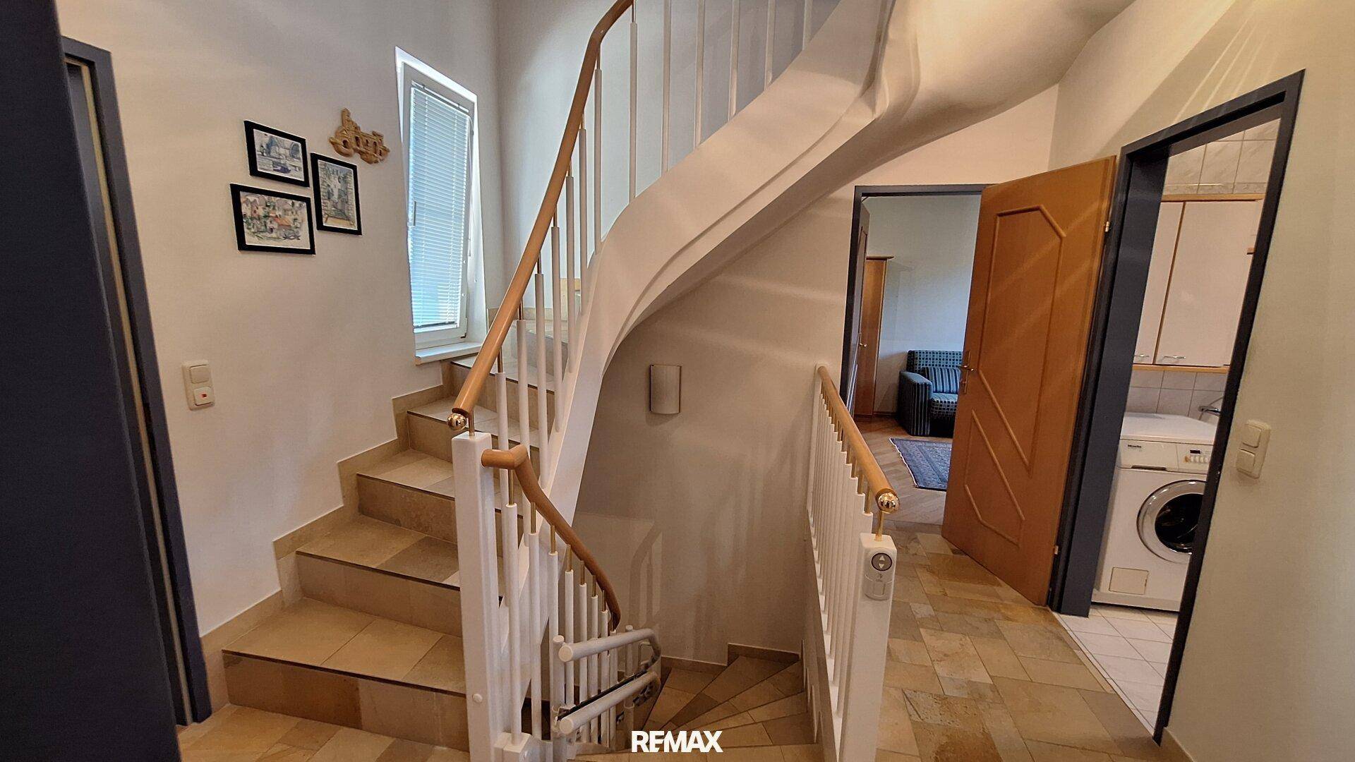 Treppenhaus mit Holzgeländer, Fliesenboden und Zugang zu weiteren Räumen.