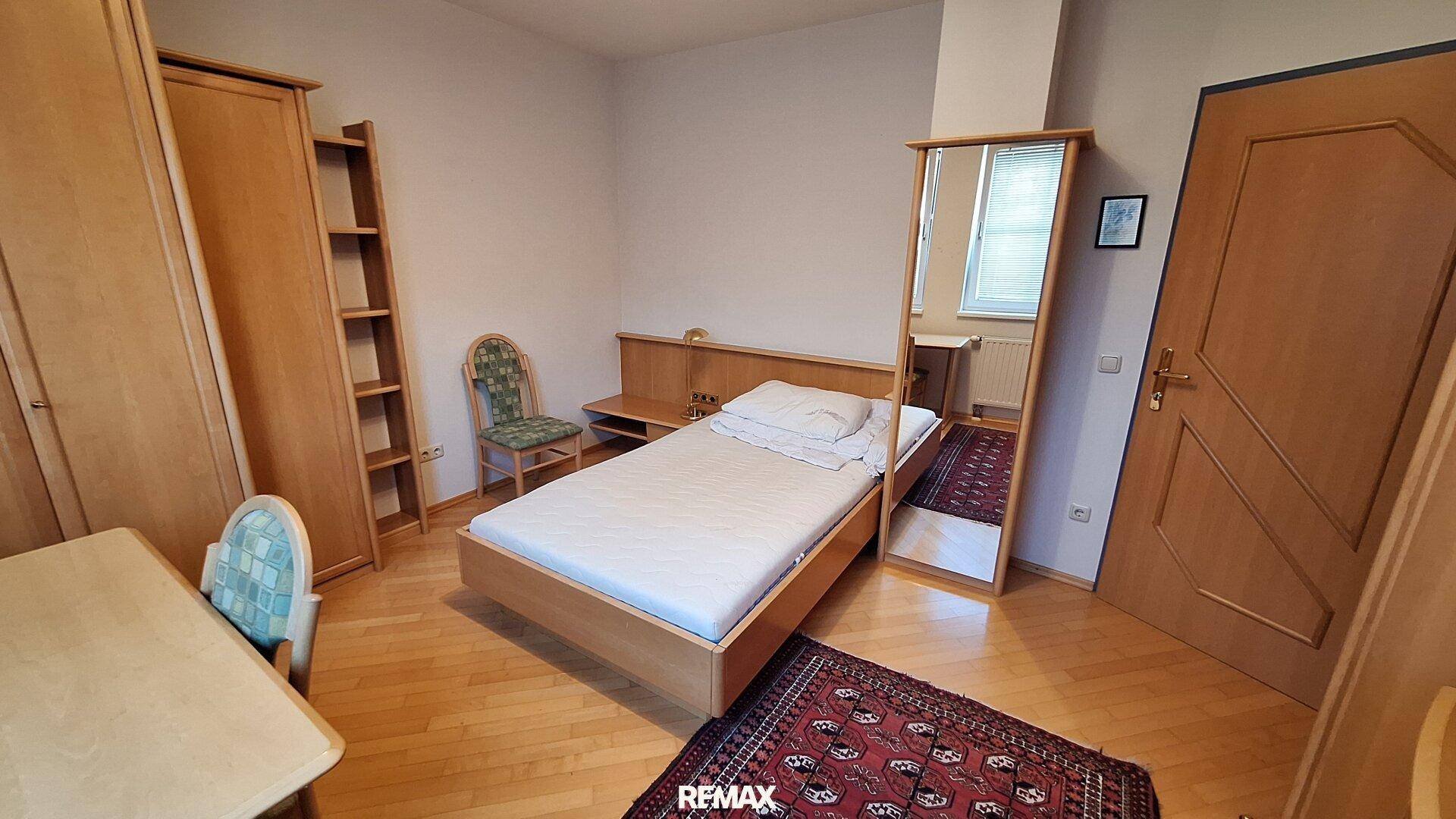 Schlafzimmer mit Einzelbett, Holzmöbeln und Teppichboden in traditionellem Stil.