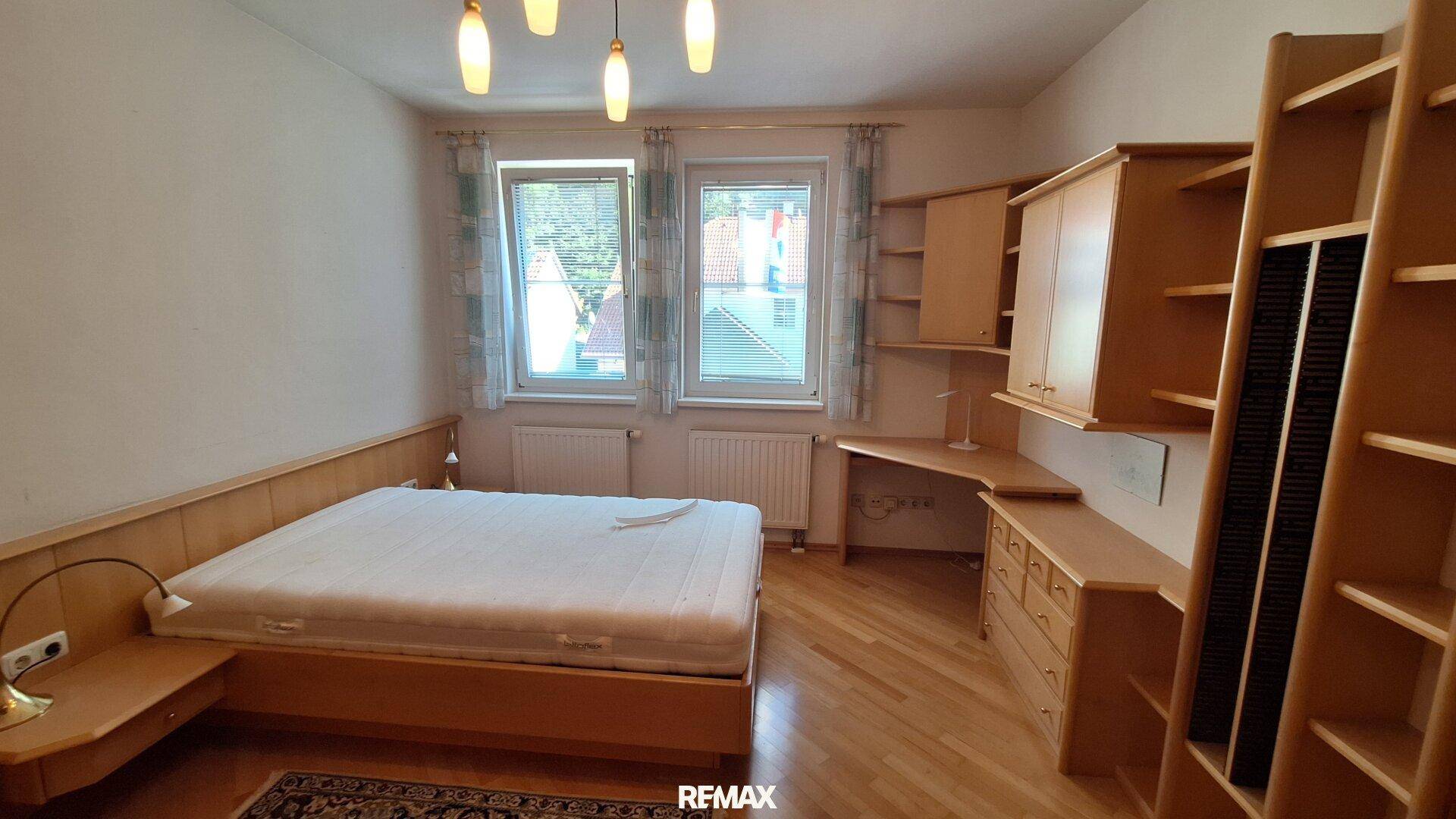 Helles Schlafzimmer mit Doppelbett, Holzmöbeln und Schreibtisch am Fenster.