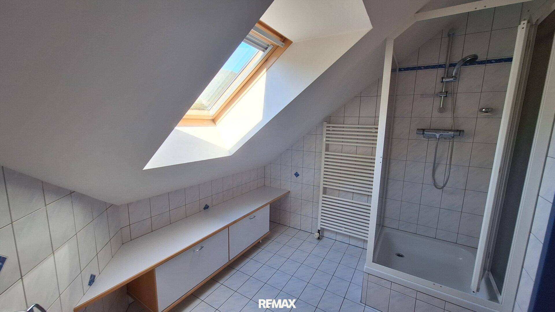 Dachgeschoss-Badezimmer mit Dusche, Handtuchheizkörper und Dachfenster.