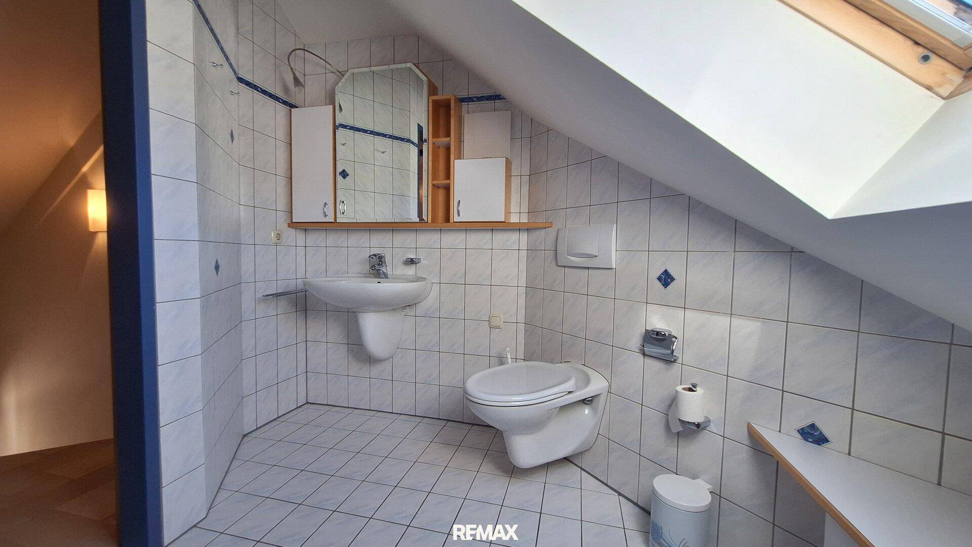 Kleines WC im Dachgeschoss mit Wand-WC, Waschbecken und Dachfenster.