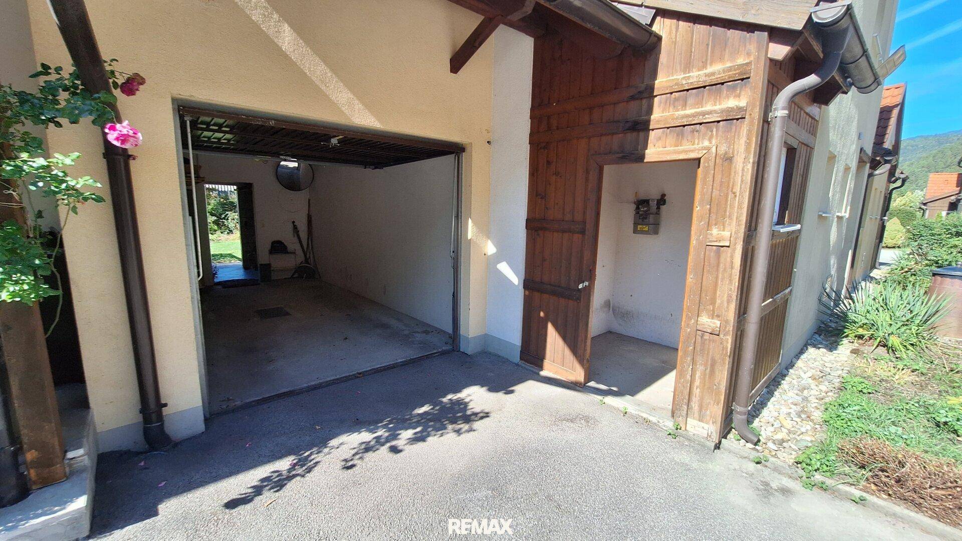 Einzelgarage mit offenem Tor und Zufahrt, umgeben von Grünflächen.