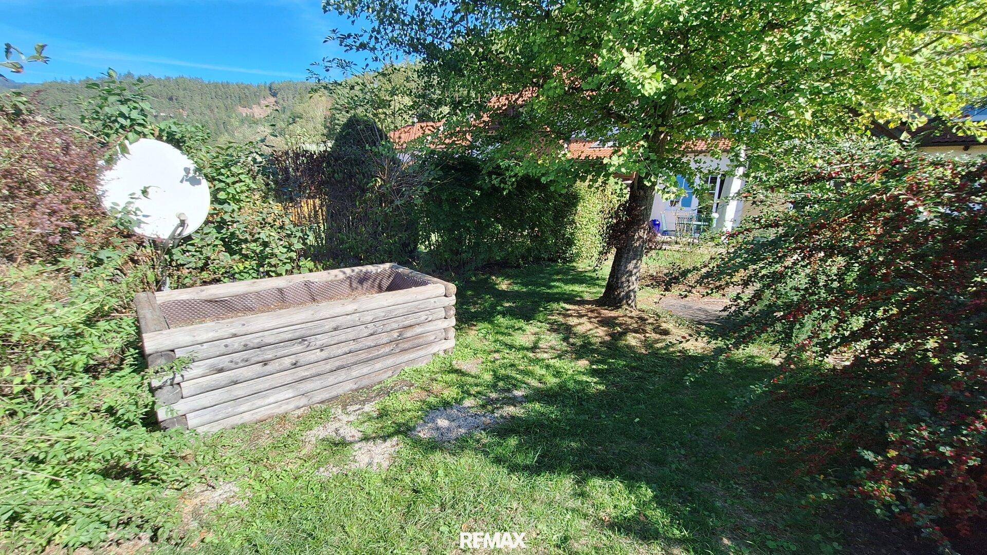Gartenbereich mit Hochbeet, Rasenfläche und Bäumen in sonniger Lage.