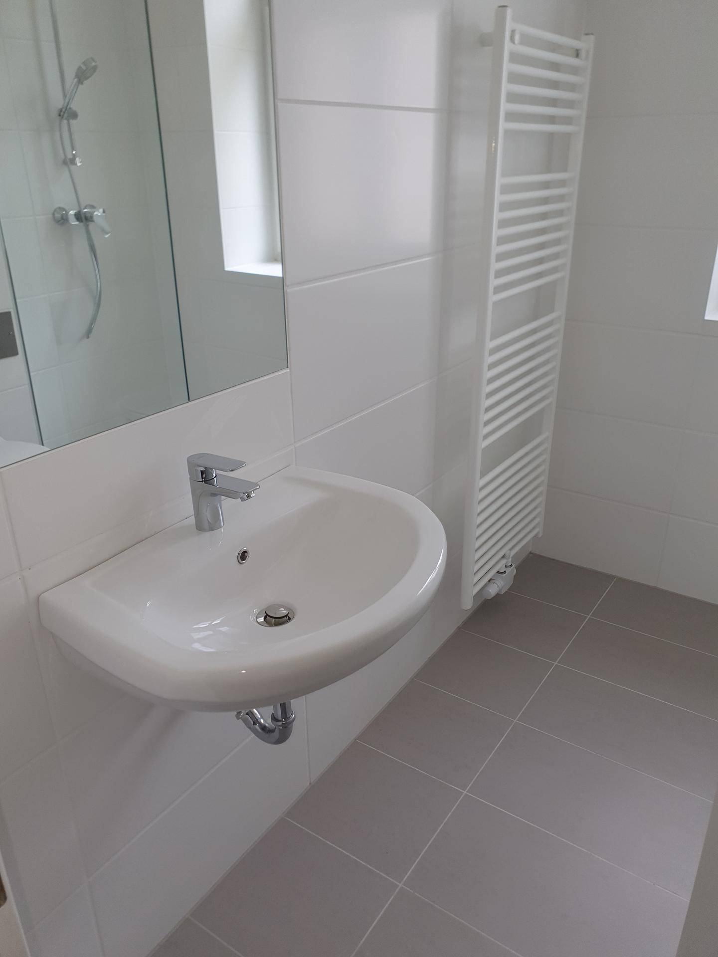 Modernes Badezimmer mit Waschbecken, Spiegel, Dusche und beheiztem Handtuchhalter.