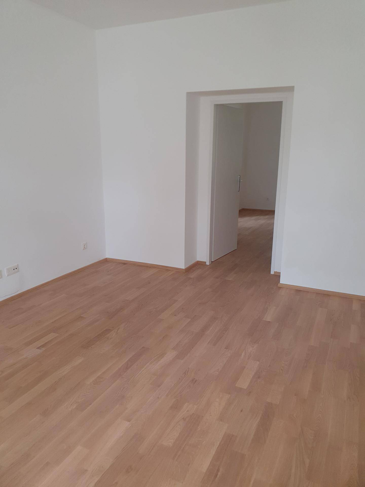 Geräumiges Zimmer mit hellem Holzparkettboden und offenem Durchgang zu einem weiteren Raum.