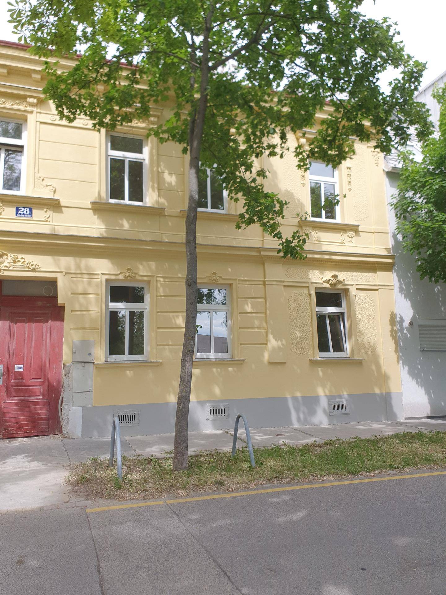 Historische gelbe Fassade eines Wohngebäudes mit weißen Fenstern und roter Eingangstür.