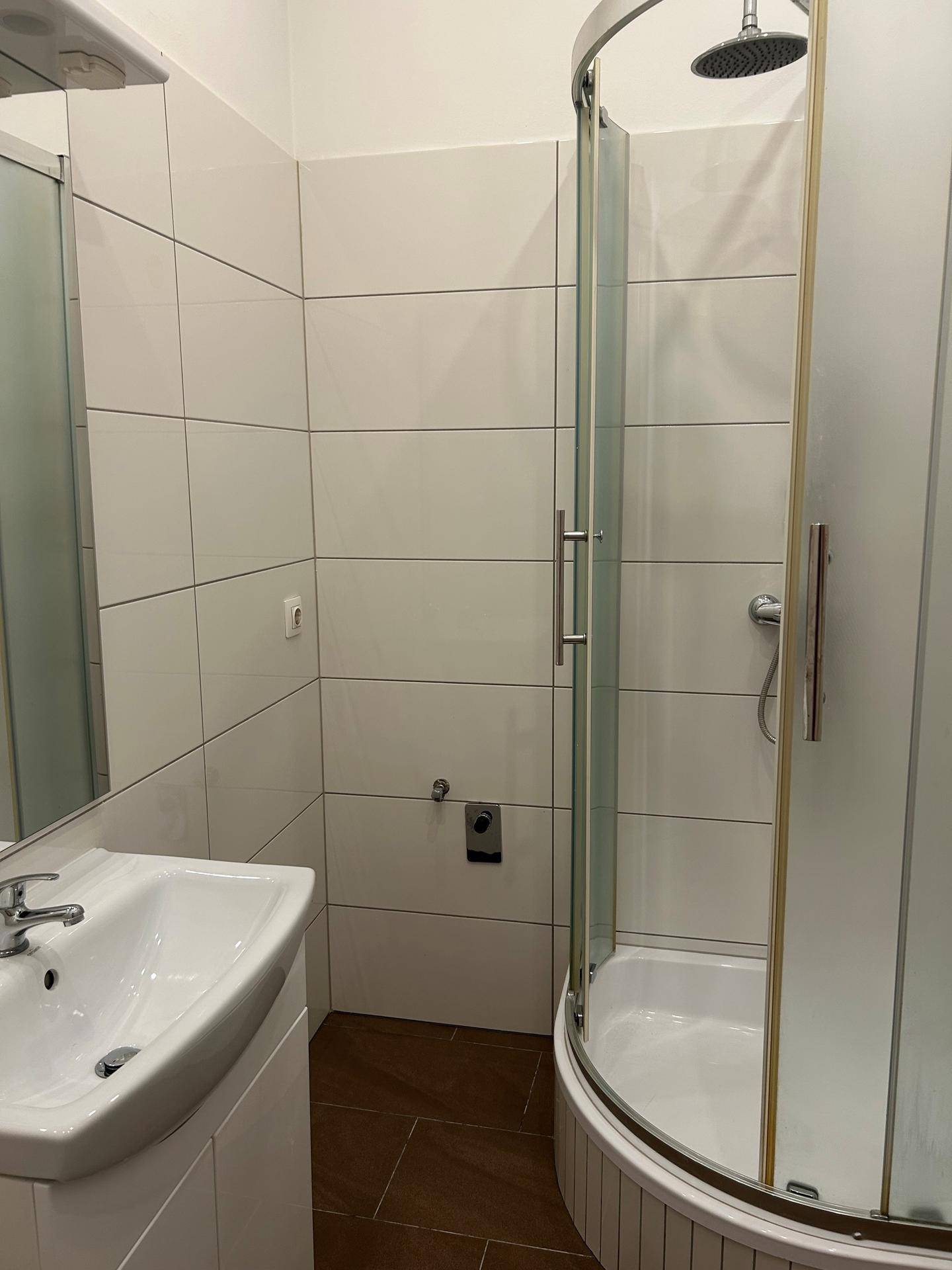 Modernes Badezimmer mit Duschkabine, Waschbecken und weißen Fliesen, in gutem Zustand.