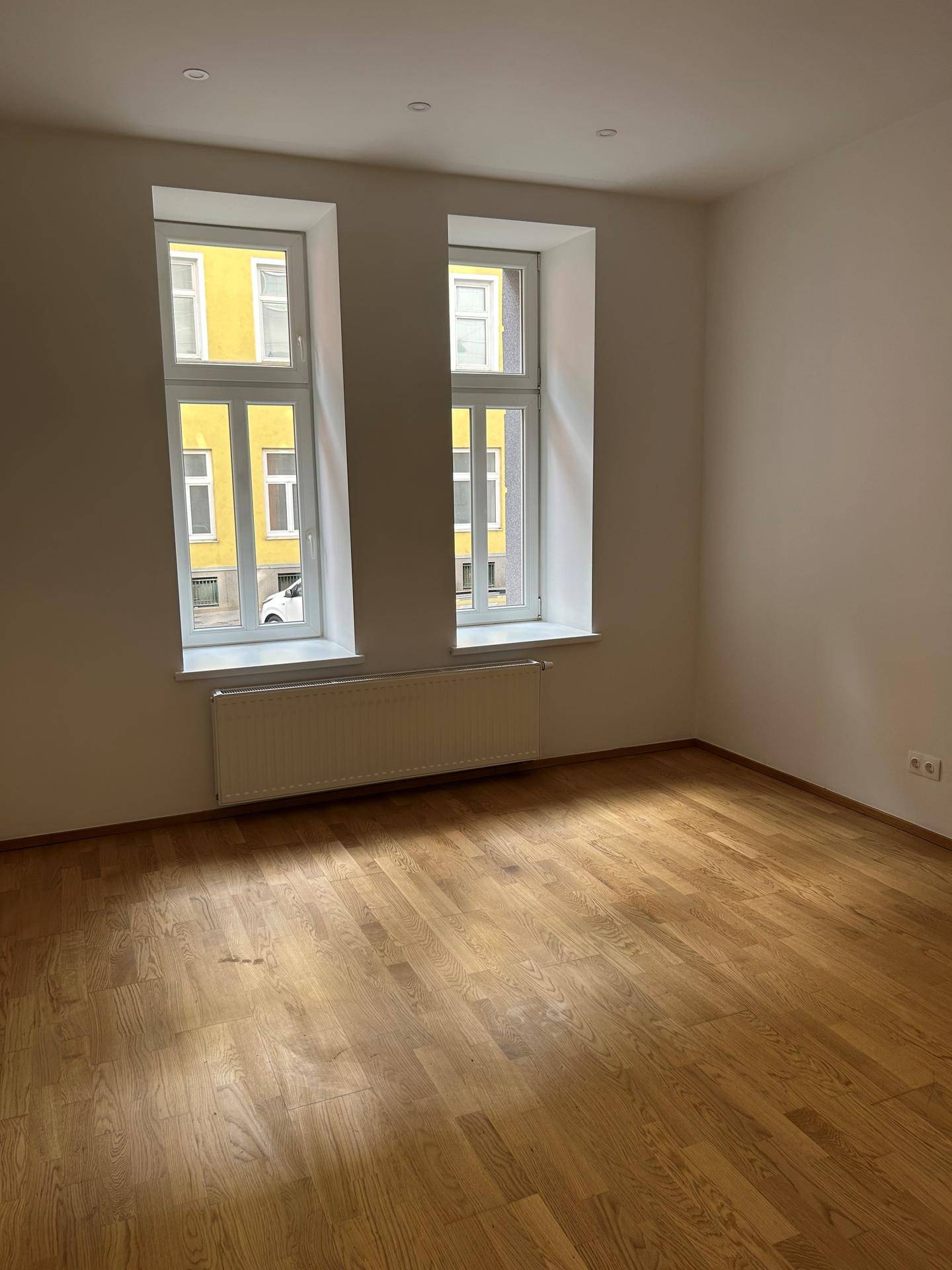 Geräumiges Zimmer mit zwei großen Fenstern, Parkettboden und viel Tageslicht, frisch gestrichen.