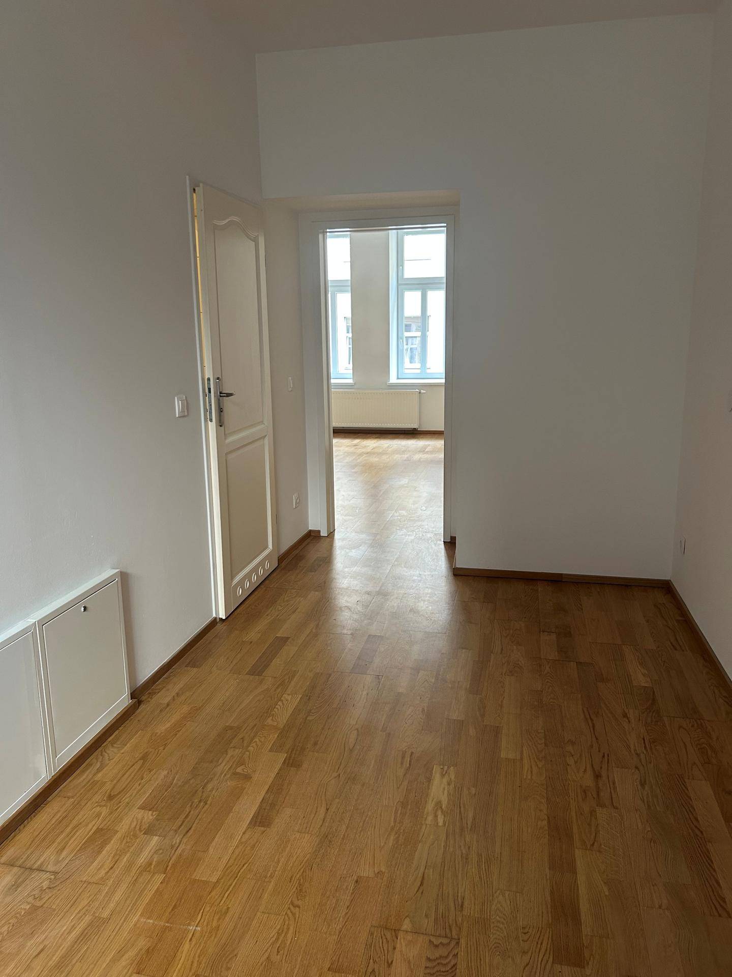 Helles Zimmer mit Parkettboden und Zugang zu einem weiteren Raum, bietet vielseitige Nutzungsmöglichkeiten.