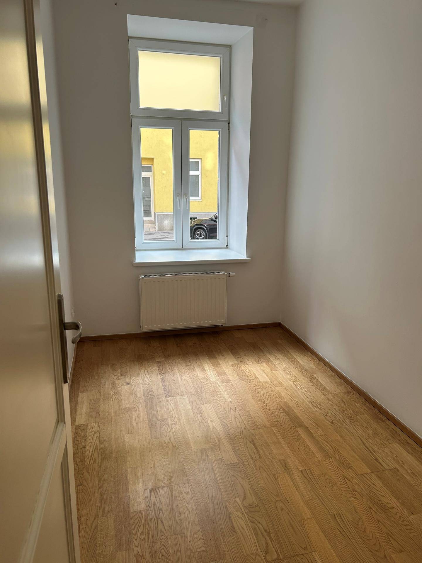 Kleineres Zimmer mit Parkettboden und einem Fenster, ideal als Schlafzimmer oder Arbeitszimmer.