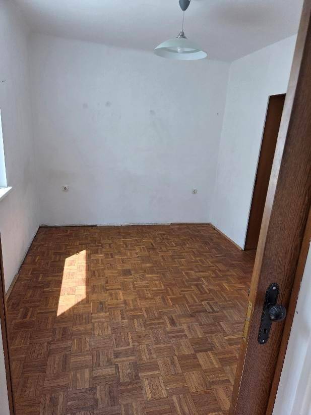 Helles Zimmer mit Parkettboden, weißen Wänden und einer einfachen Deckenleuchte.