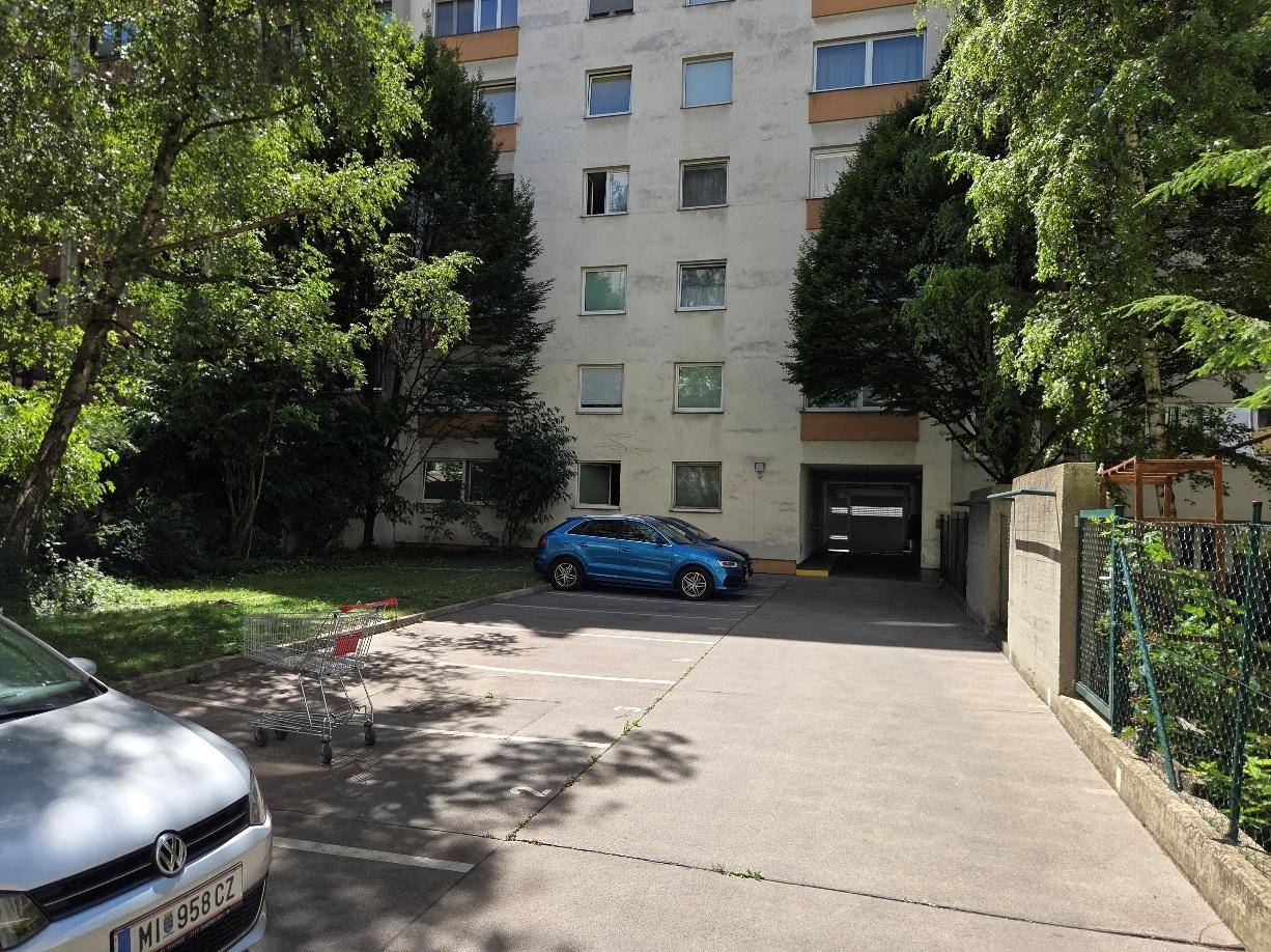 Außenbereich eines Wohngebäudes mit Parkplätzen und viel Grün in der Umgebung.