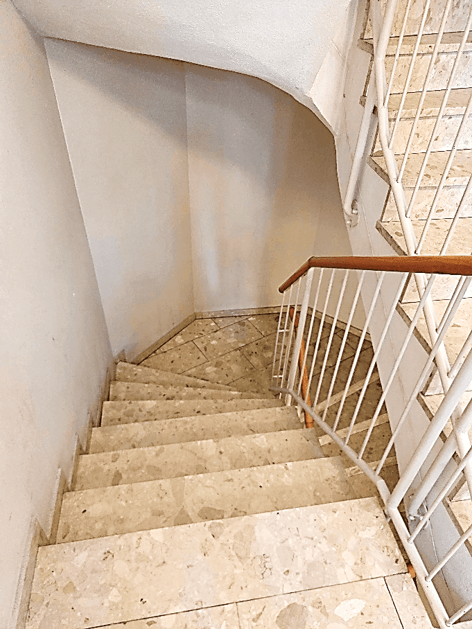 Treppenhaus mit Marmorstufen und einem Geländer aus Metall und Holzhandlauf.