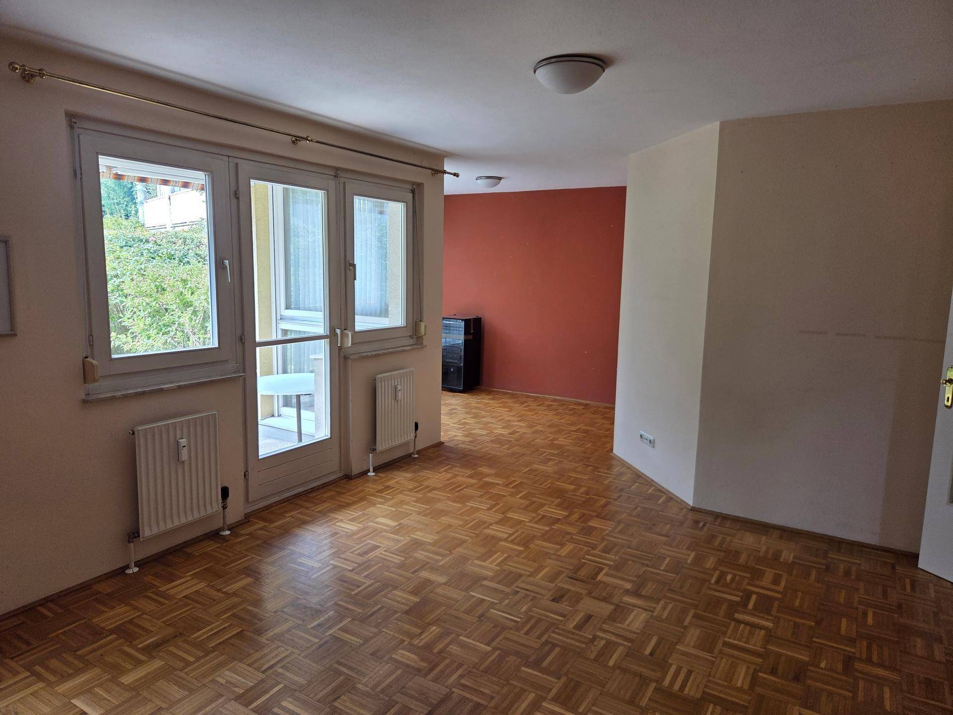 Wohnbereich mit Parkettboden, Zugang zur Terrasse und einer farbigen Akzentwand.