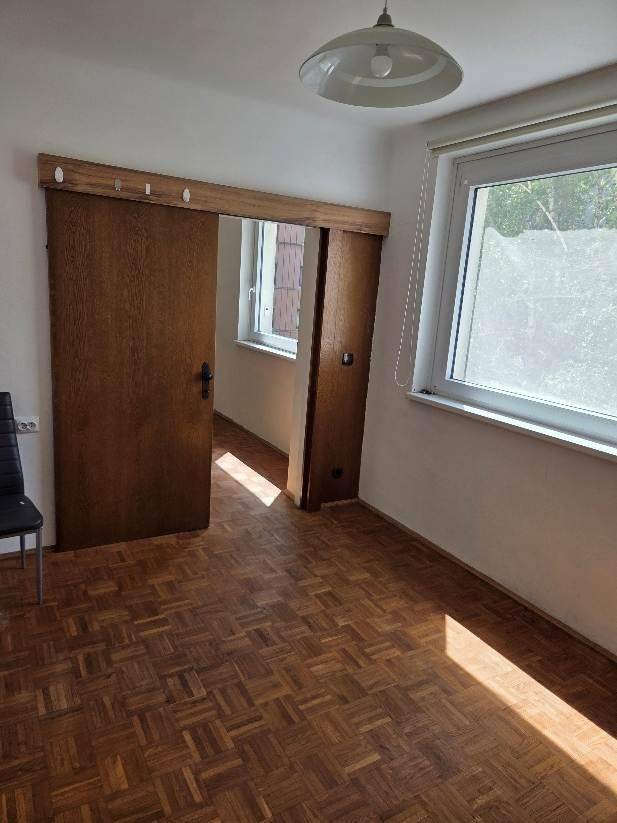 Zimmer mit Parkettboden, Fenster und einer praktischen Holzschiebetür.