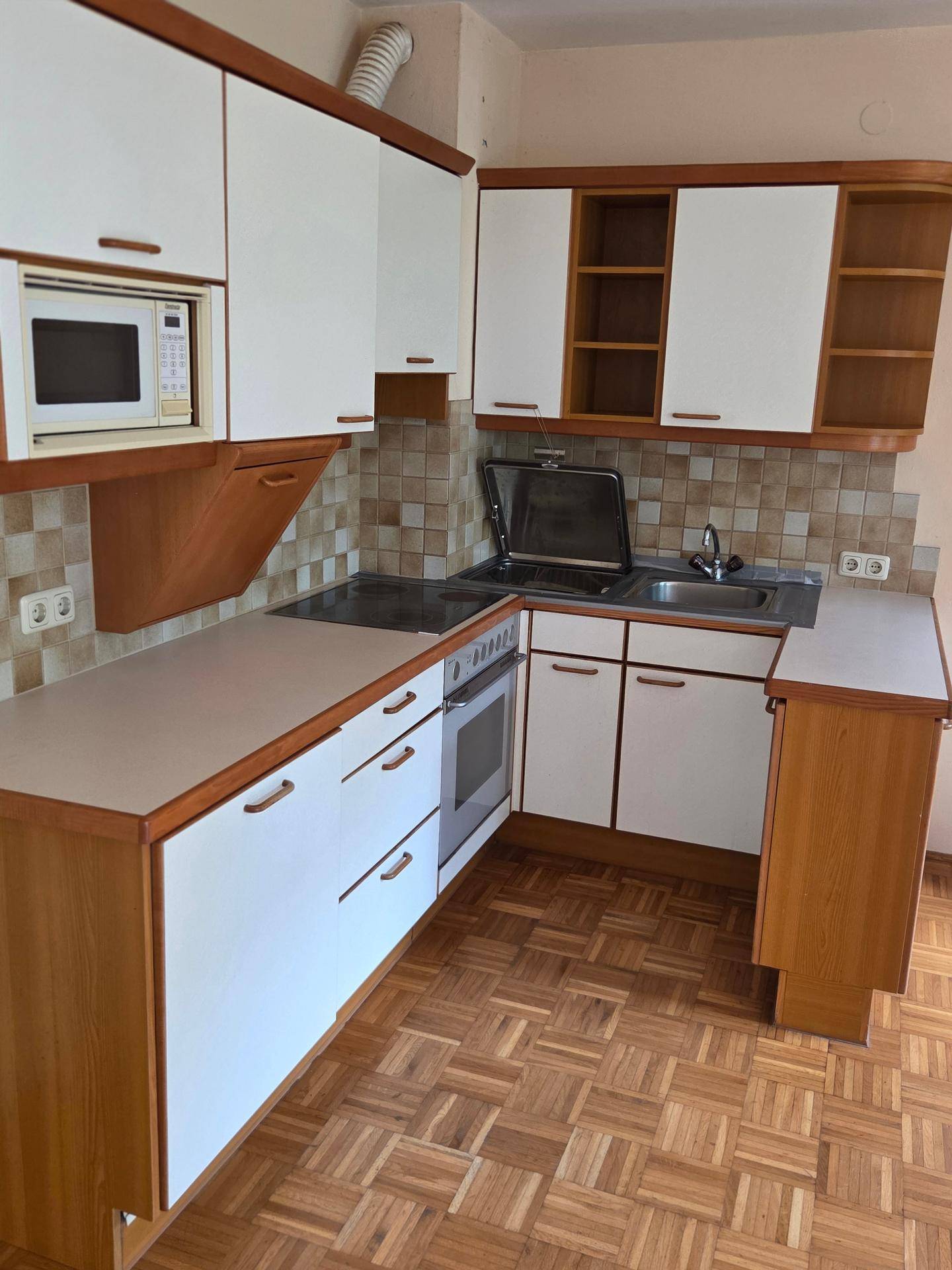 Funktionale Küche mit weißen und holzfarbenen Schränken, Mikrowelle und Fliesenrückwand.