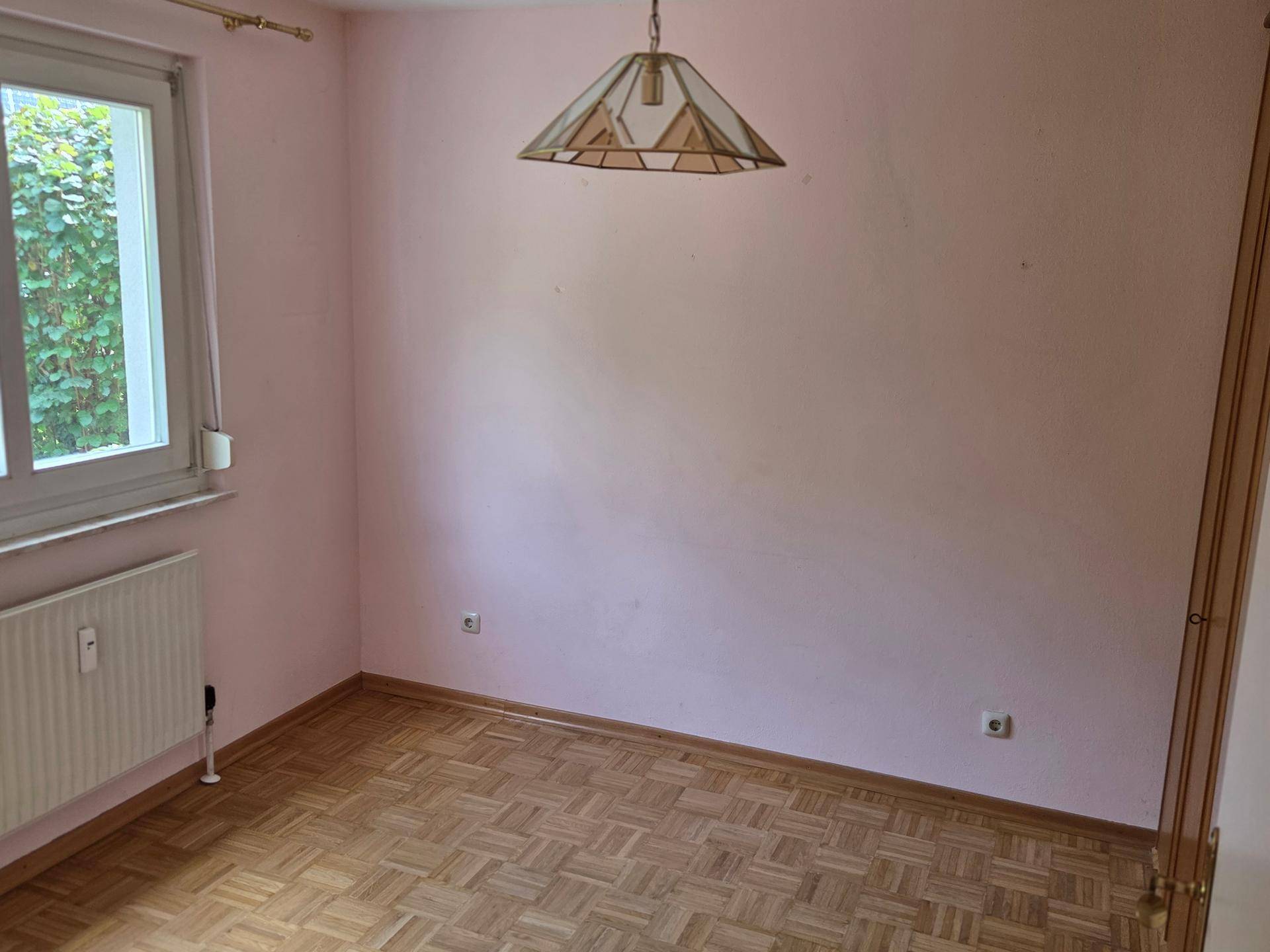 Helles Schlafzimmer mit rosa Wänden, Parkettboden und Fenster mit Blick ins Grüne.