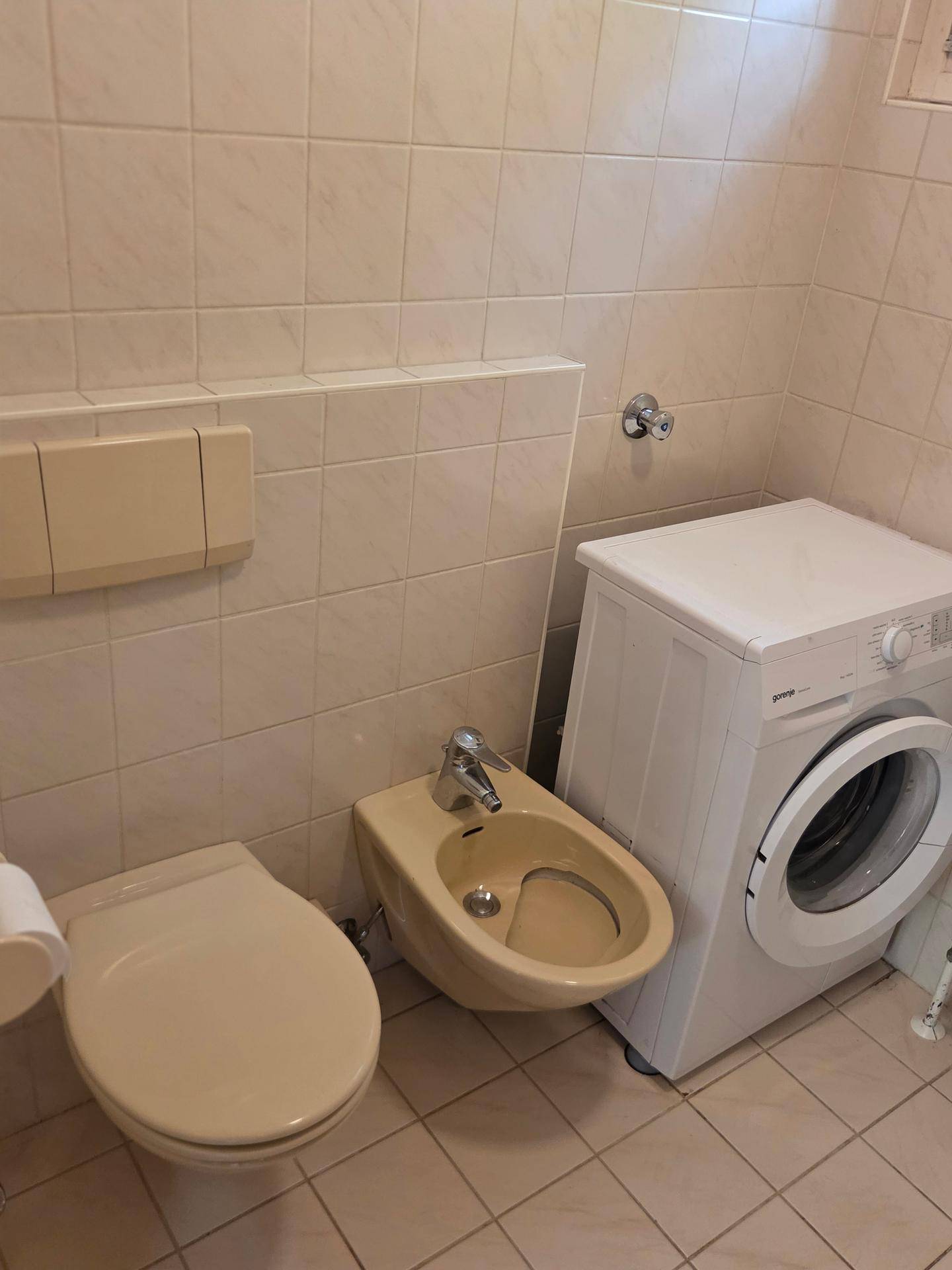 Badezimmer mit Fliesen, Toilette, Bidet und einer Waschmaschine.