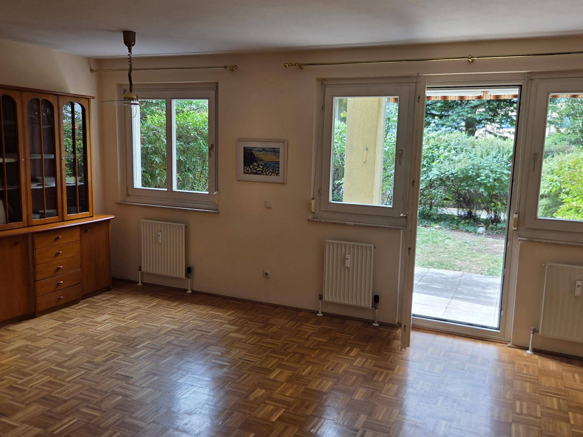 Helles Wohnzimmer mit Parkettboden, großen Fenstern und Zugang zur Terrasse und zum Garten.