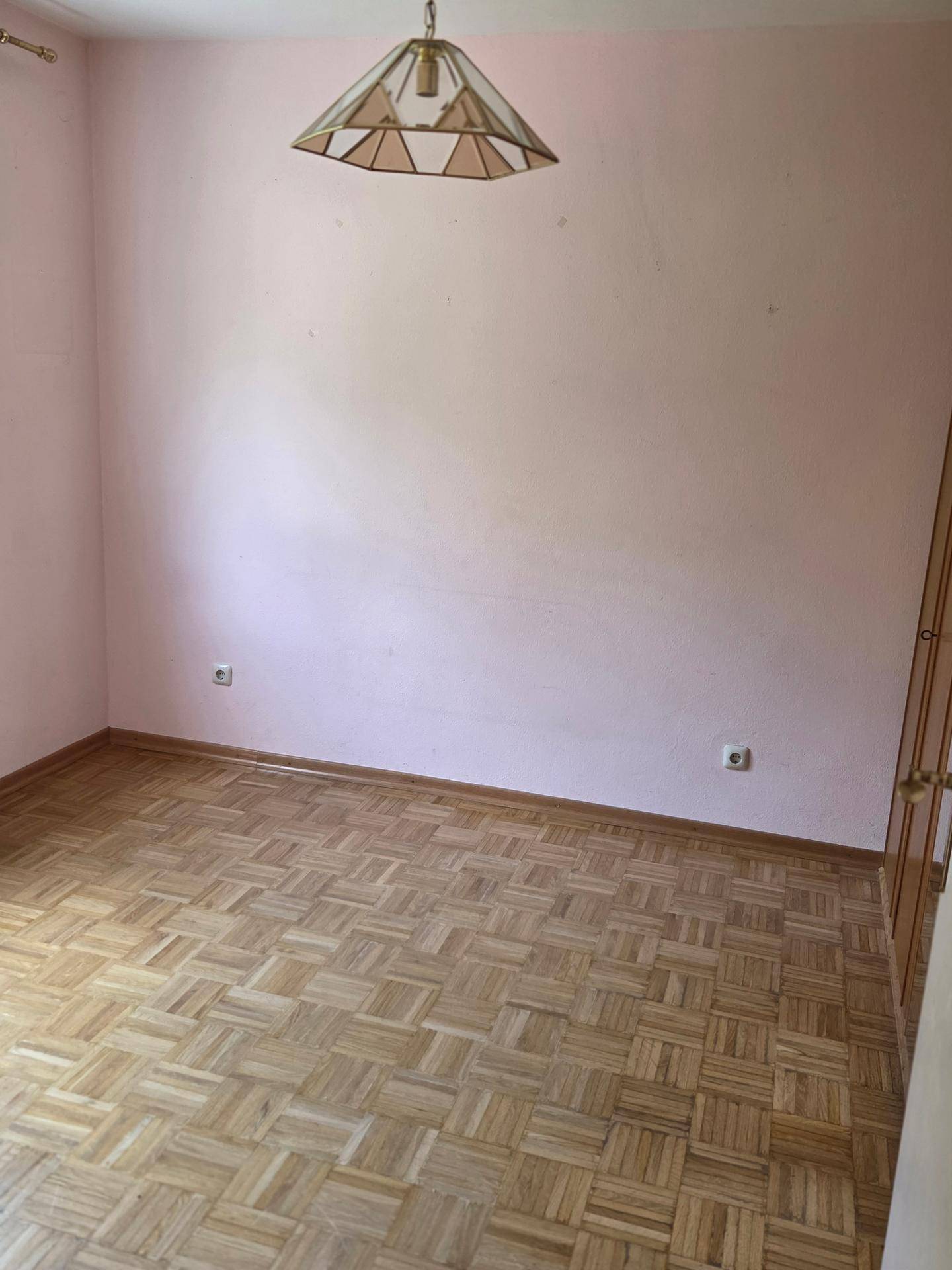 Leeres Schlafzimmer mit rosa Wänden, Parkettboden und einer Deckenleuchte.