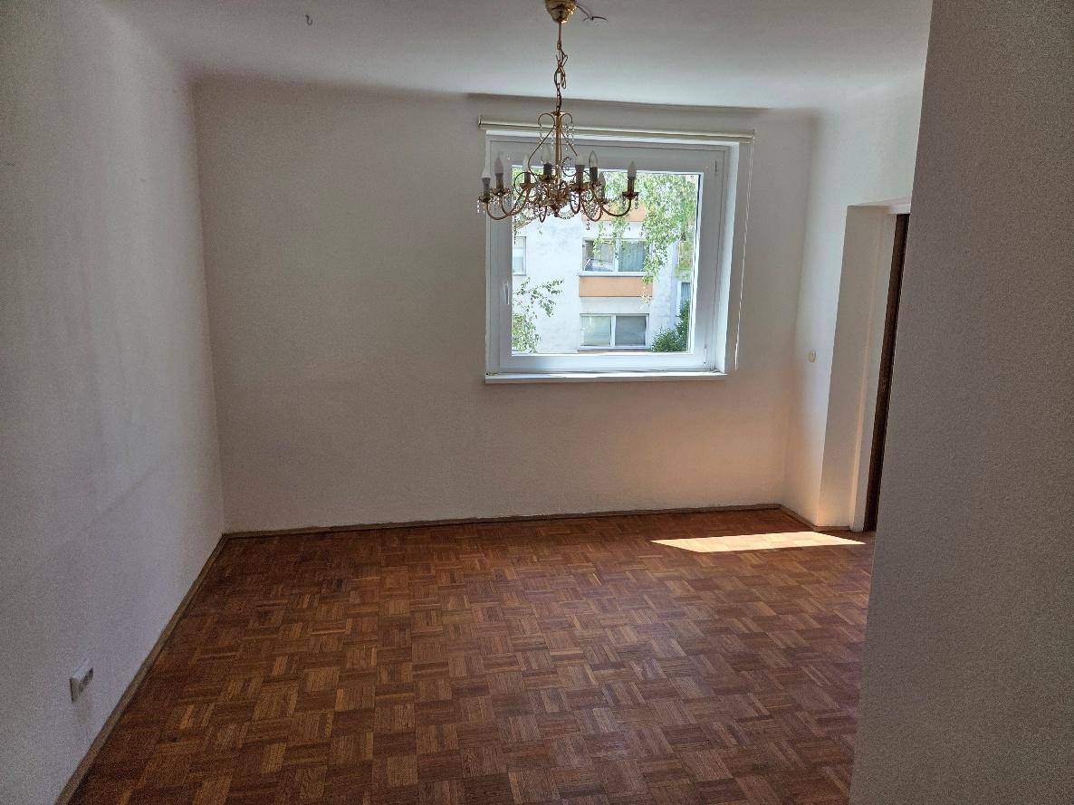 Geräumiges Zimmer mit Parkettboden, Kronleuchter und einem Fenster mit Blick auf die Umgebung.