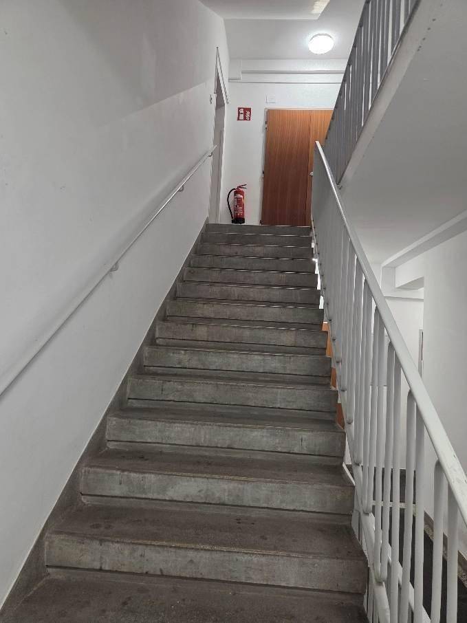 Treppenhaus mit Steinstufen und Metallgeländer, das die Stockwerke verbindet.