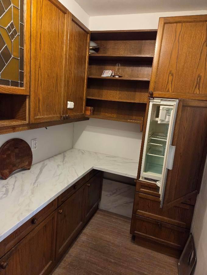 Kleine Küche mit Holzschränken, weißer Arbeitsplatte und integriertem Kühlschrank.