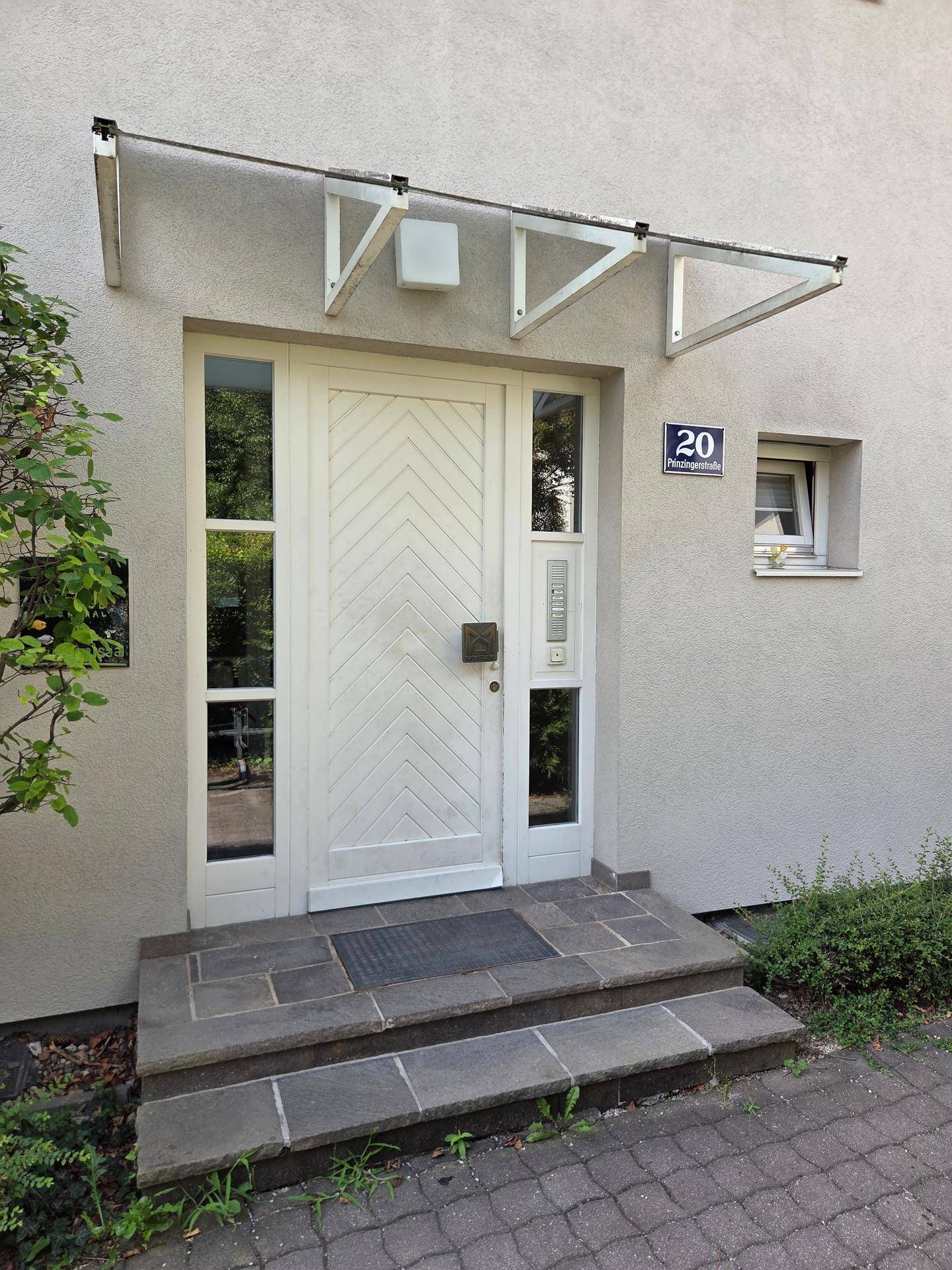 Haupteingang des Gebäudes mit weißer Tür, Glasvordach und Hausnummer 20.