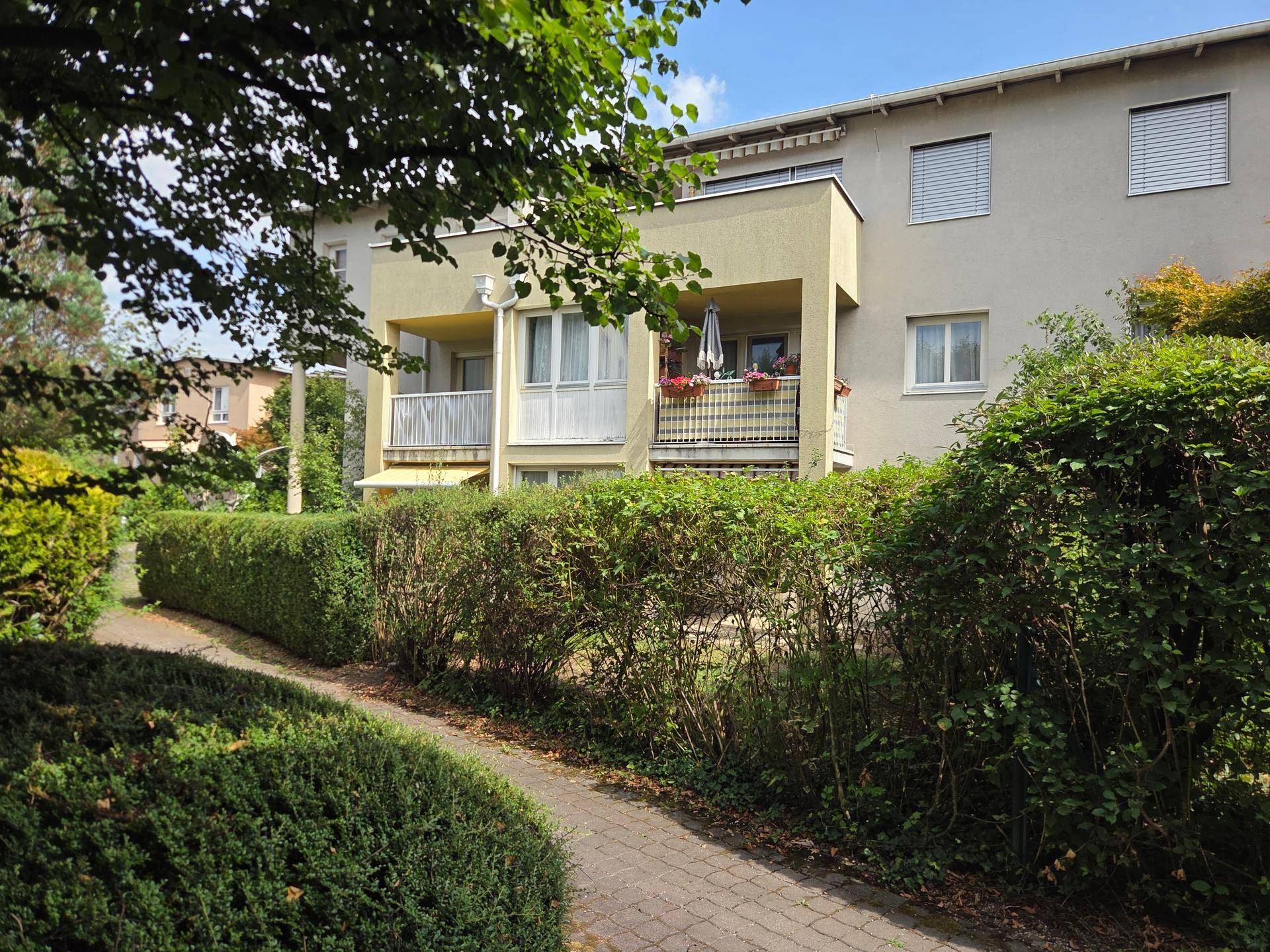 Mehrfamilienhaus mit Balkonen, umgeben von grünen Hecken und Bäumen in ruhiger Lage.