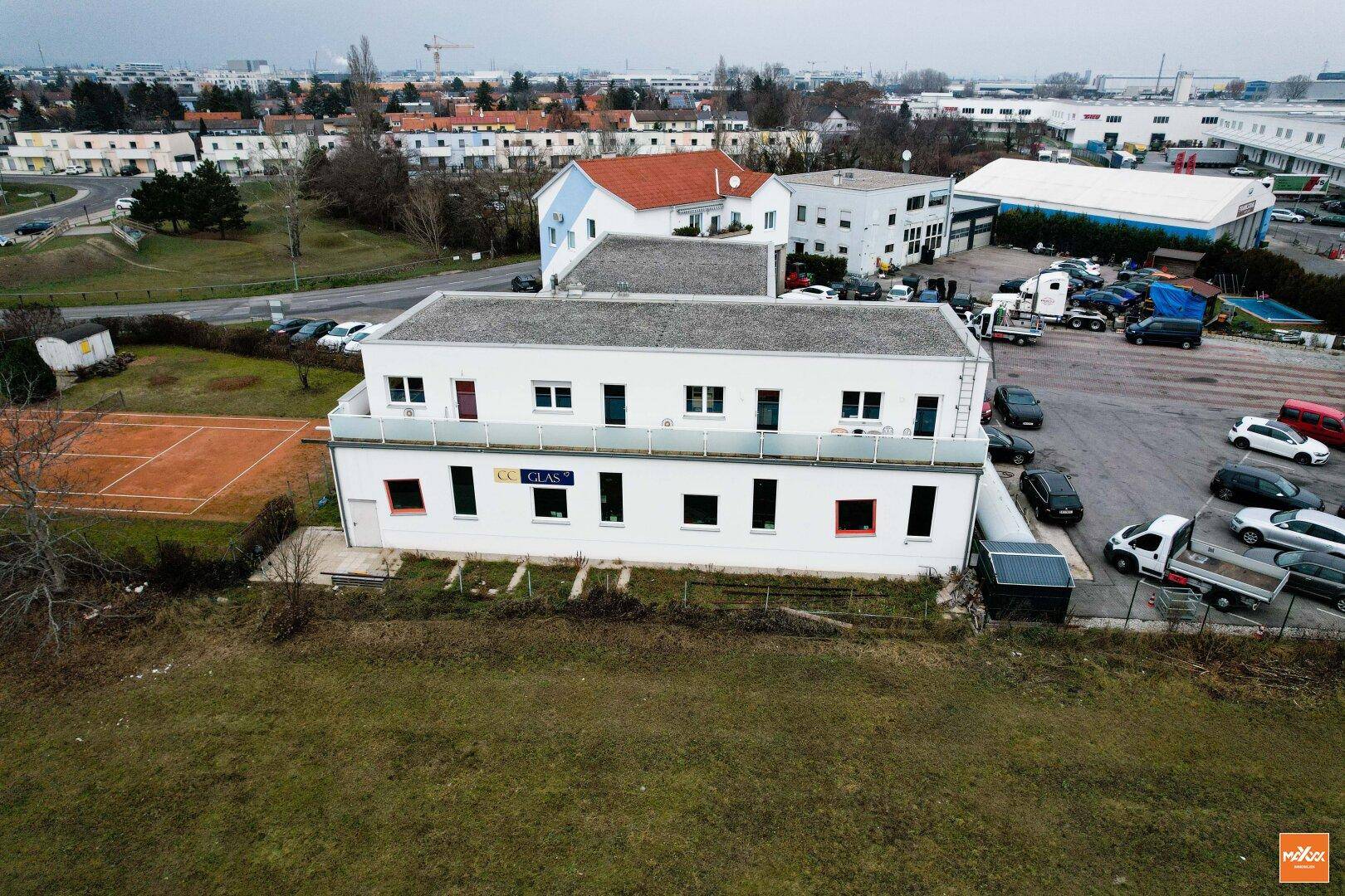 Rückansicht des Bürogebäudes mit Flachdach, Fenstern und einem Tennisplatz im Vordergrund.
