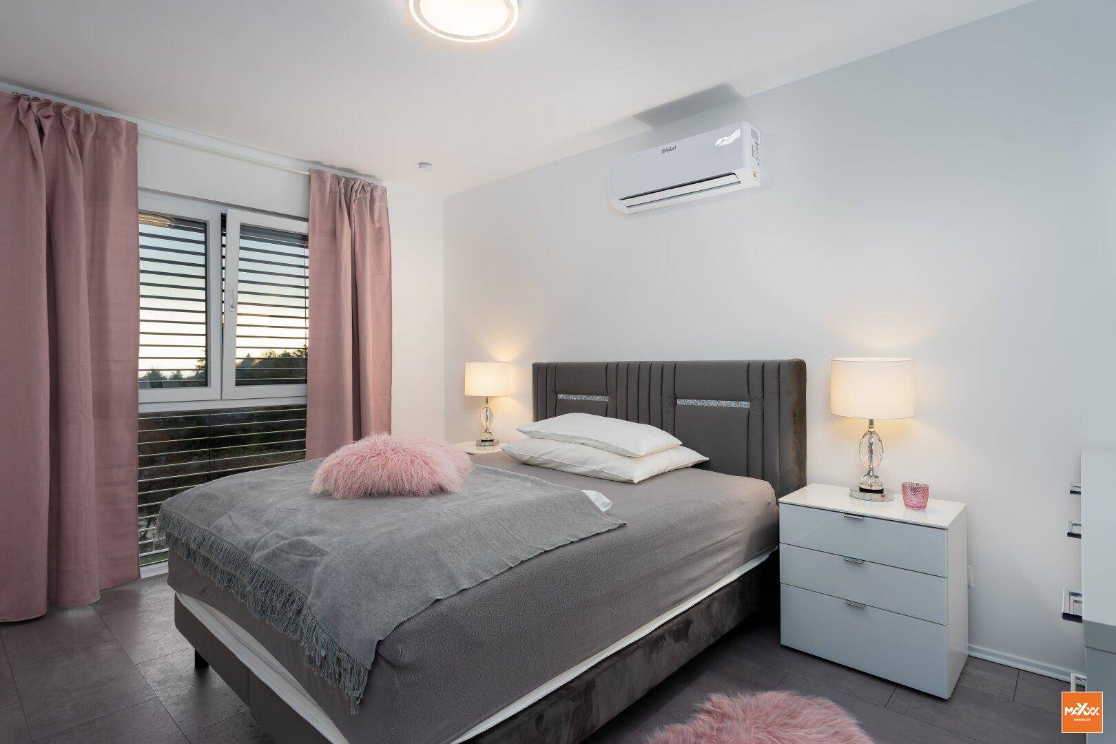 Helles Schlafzimmer mit Doppelbett, rosa Vorhängen und Klimaanlage.