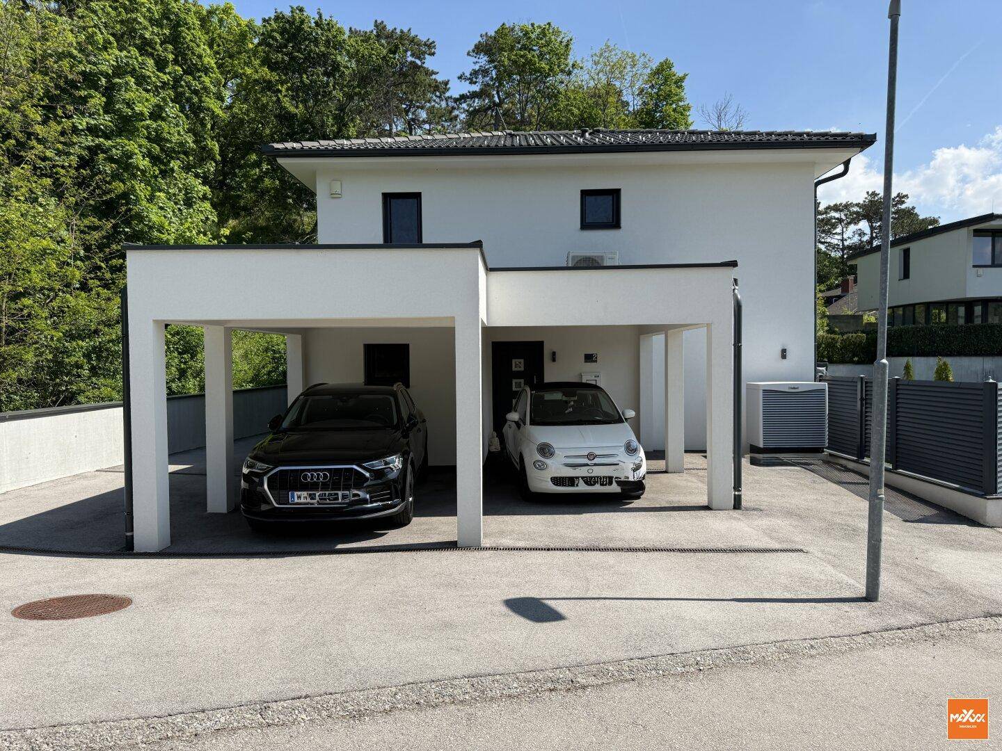 Moderne Hausfassade mit Doppelcarport und zwei Stellplätzen, umgeben von grüner Natur.