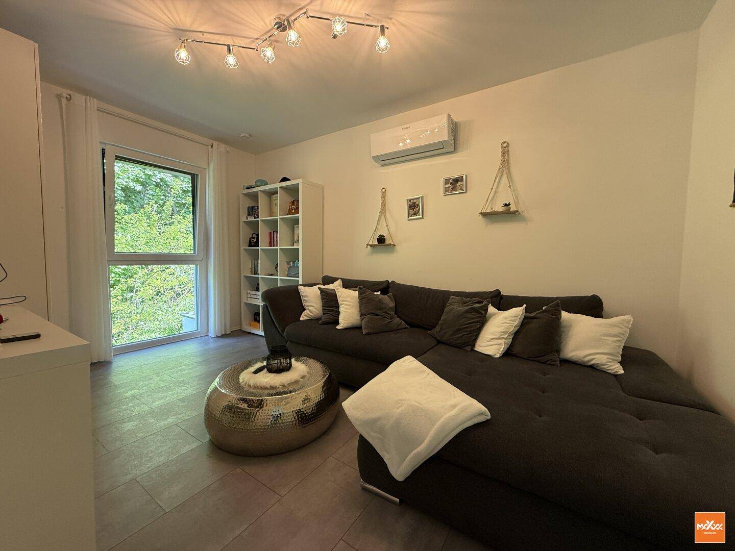Modern eingerichtetes Schlafzimmer mit großem Sofa, Klimaanlage und Fenster zum Garten.