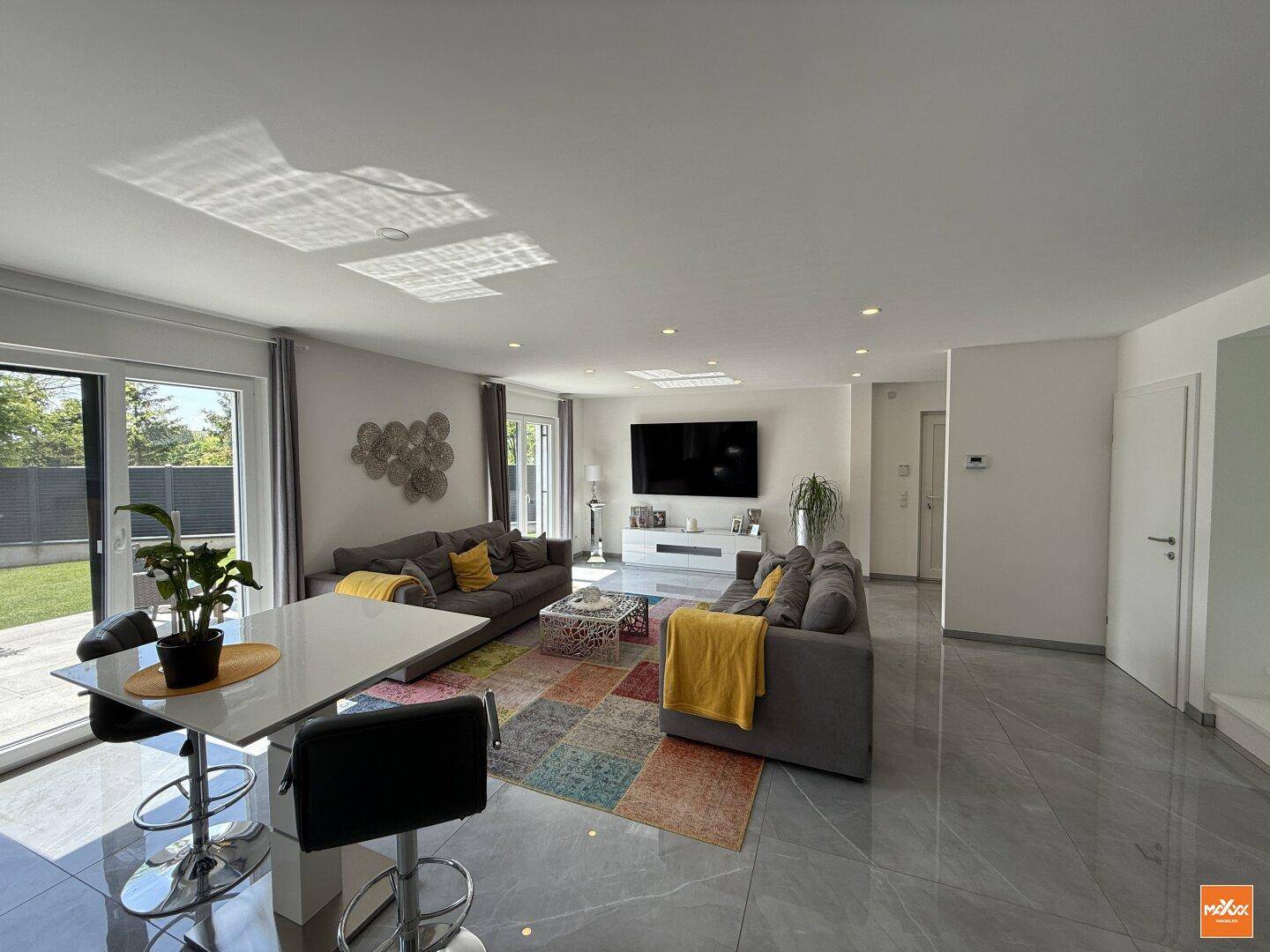 Heller Wohn- und Essbereich mit großformatigen Fliesen, bequemen Sofas und Zugang zur Terrasse.