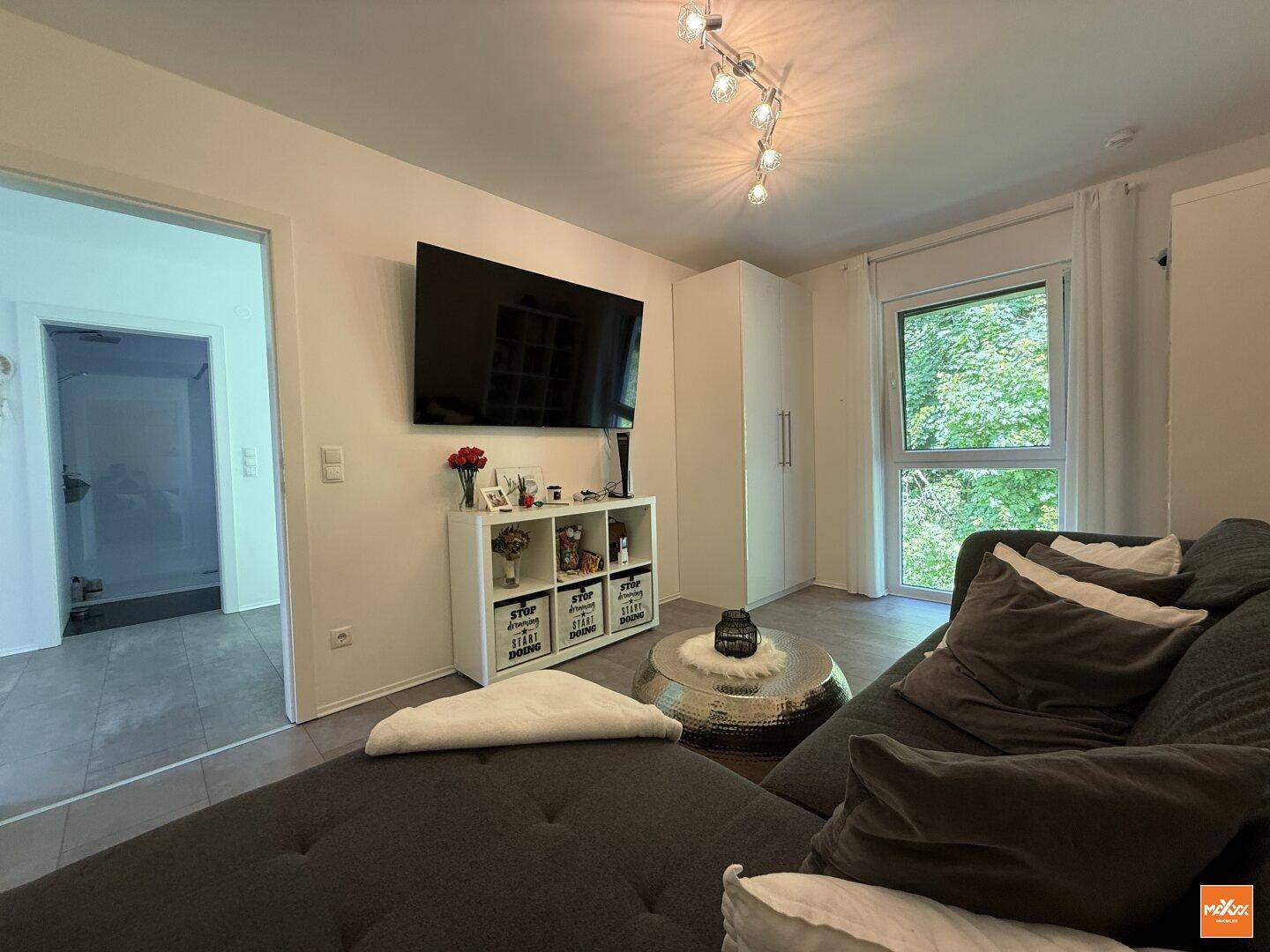 Gemütliches Schlafzimmer mit großem Fernseher, modernem Sofa und Blick ins Grüne.