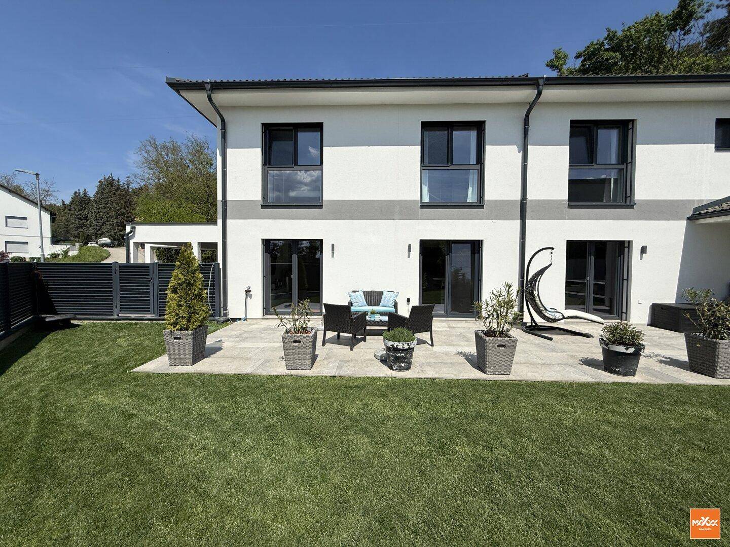 Sonniger Terrassenbereich mit modernen Gartenmöbeln und direktem Zugang zum grünen Rasen.