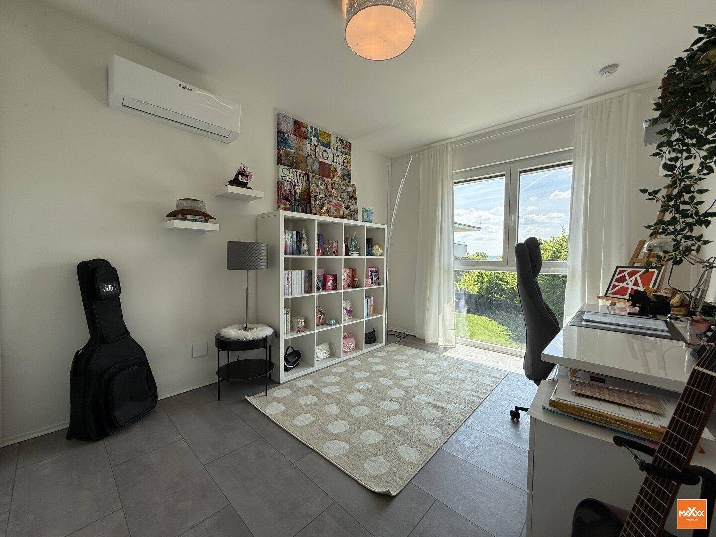 Helles Arbeitszimmer mit großem Fenster, Bücherregal und Klimaanlage, ideal für Home-Office.