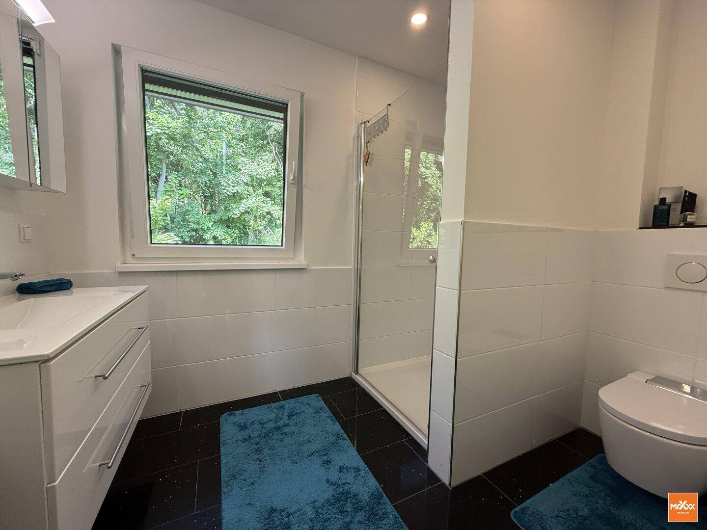 Modernes Badezimmer mit Dusche, Waschtisch und Fenster mit Blick ins Grüne.