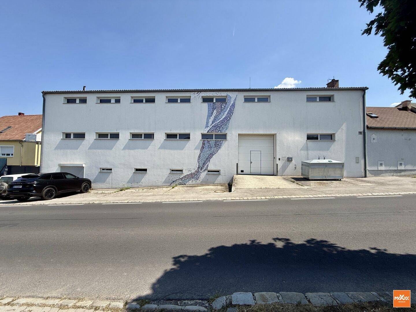 Fassade eines Gebäudes mit großer Garageneinfahrt und künstlerischem Mosaik an der Wand.