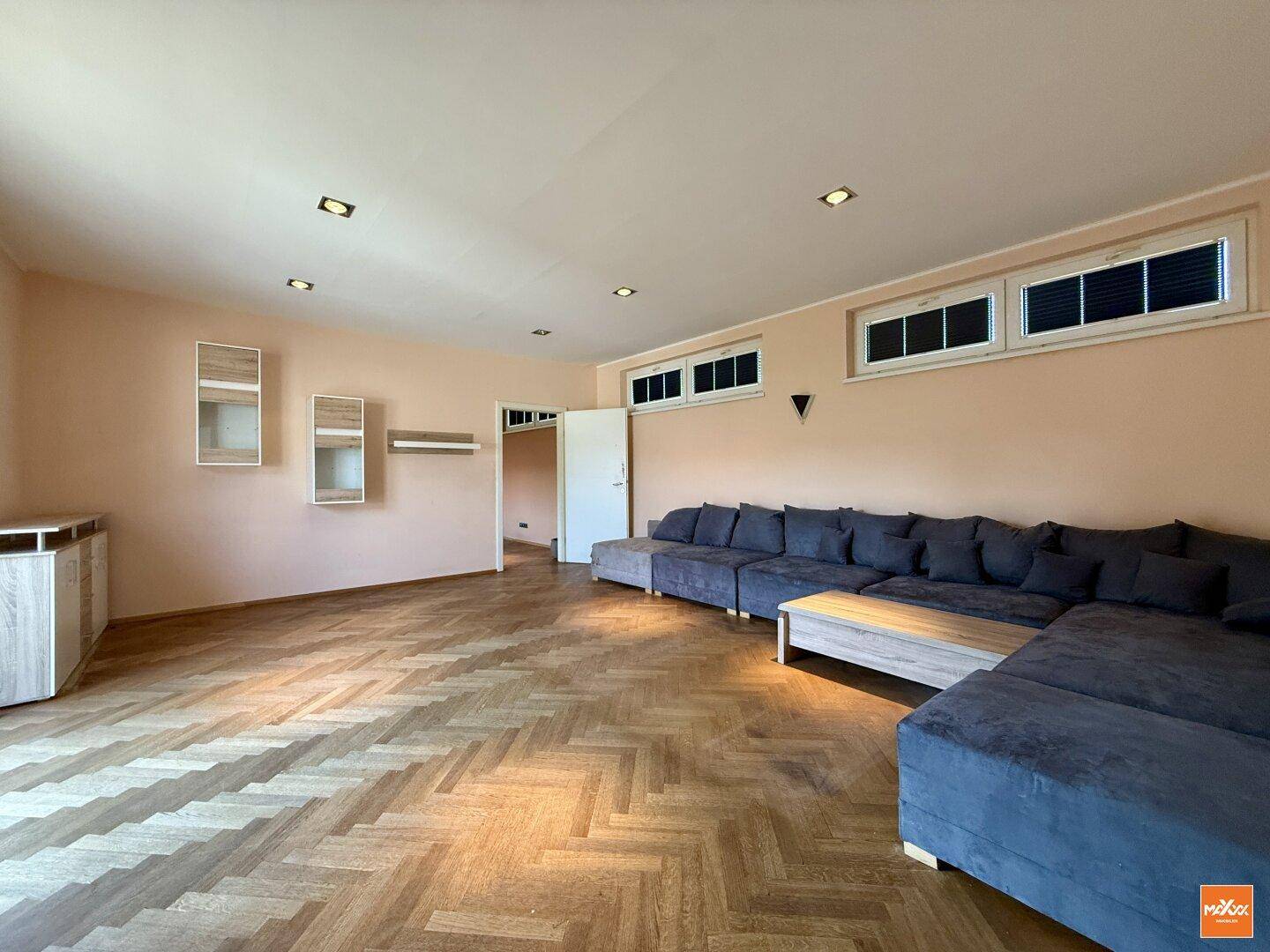 Gemütliches Wohnzimmer mit großem Ecksofa, Fischgrätparkett und indirekter Deckenbeleuchtung.