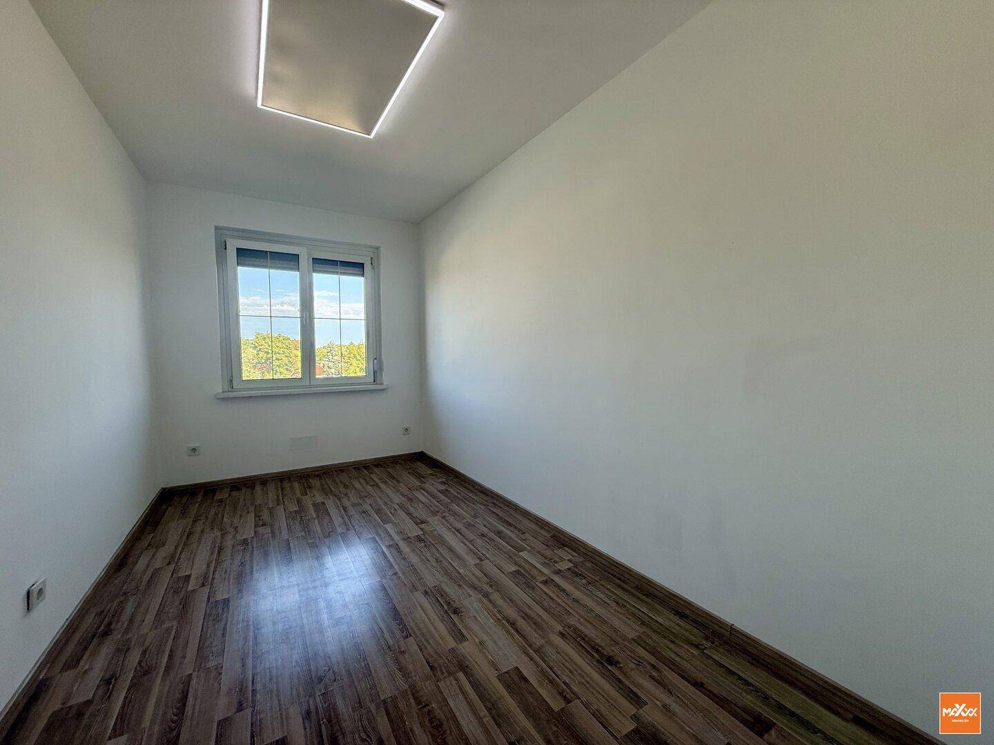 Helles Zimmer mit Laminatboden und einem Fenster, ideal als Schlaf- oder Arbeitszimmer.