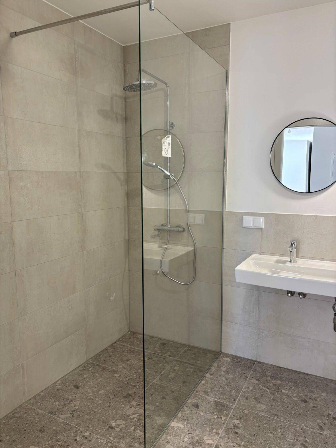 Modernes Badezimmer mit begehbarer Dusche, einzelnen Waschbecken und hellen Fliesen.