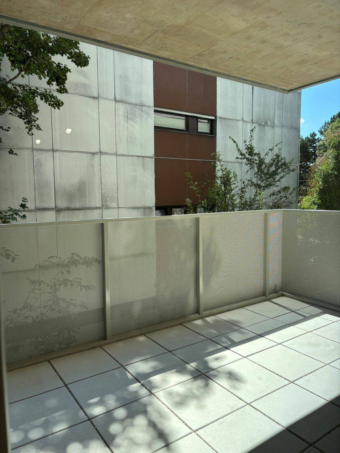 Gefliester Balkon mit moderner Brüstung und Blick auf die umliegenden Gebäude und Bäume.