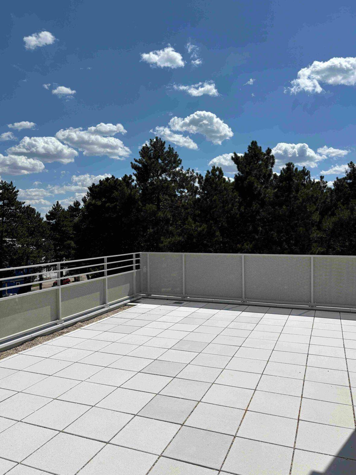 Große, geflieste Dachterrasse mit weitem Blick ins Grüne unter blauem Himmel.