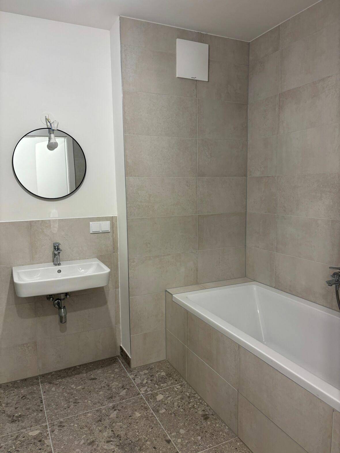 Helles Badezimmer mit Badewanne, modernem Waschbecken und rundem Spiegel.
