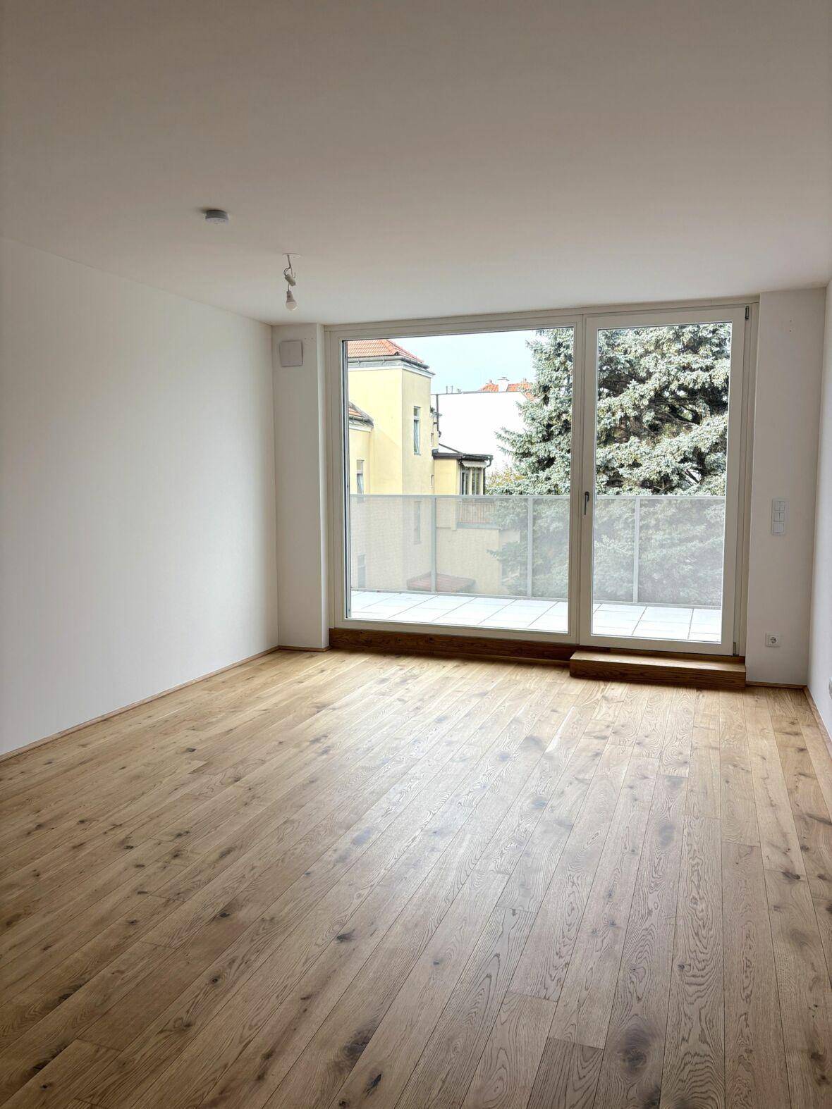 Heller Wohnraum mit Eichenparkettboden und direktem Zugang zu einem Balkon.