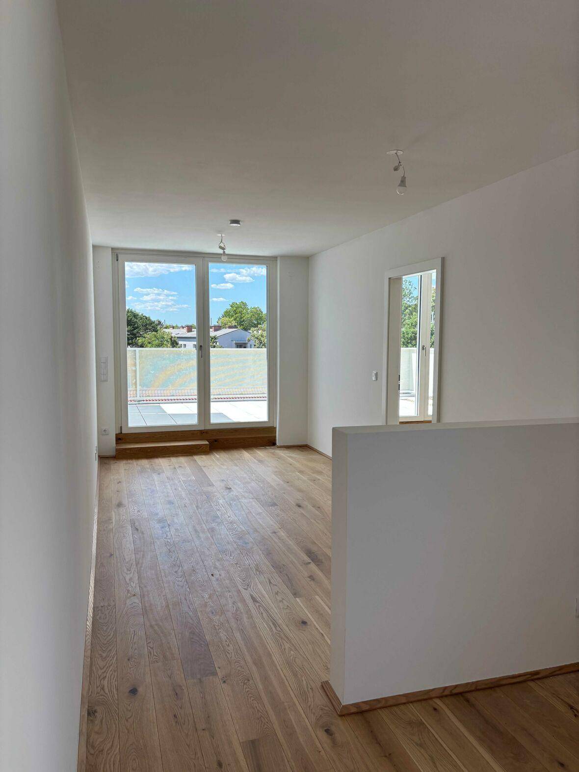 Heller Flur mit Holzboden und großen Glastüren, die zu einer Außenterrasse führen.