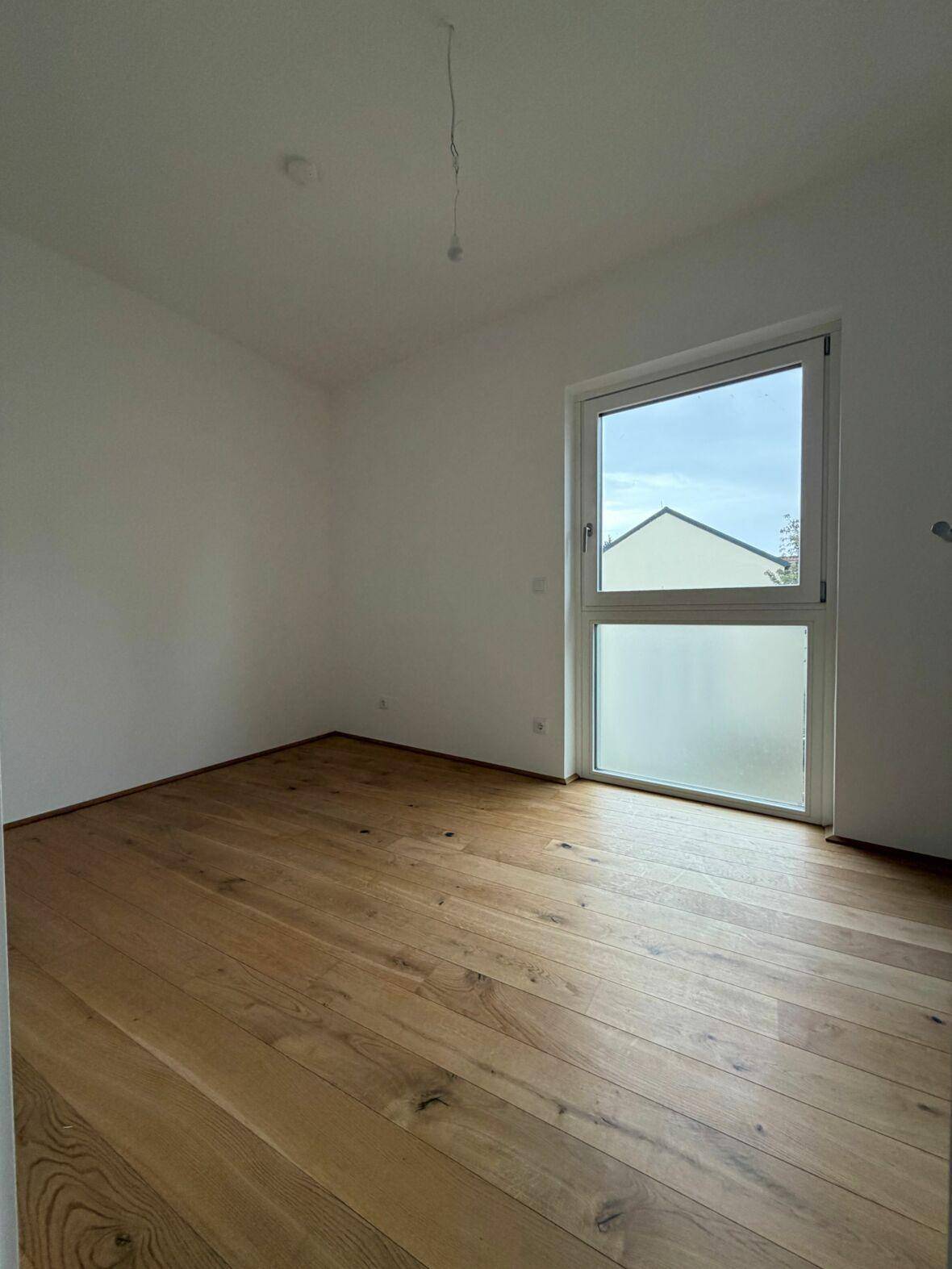 Lichtdurchfluteter Raum mit neuem Holzboden und Blick auf die Umgebung durch das Fenster.